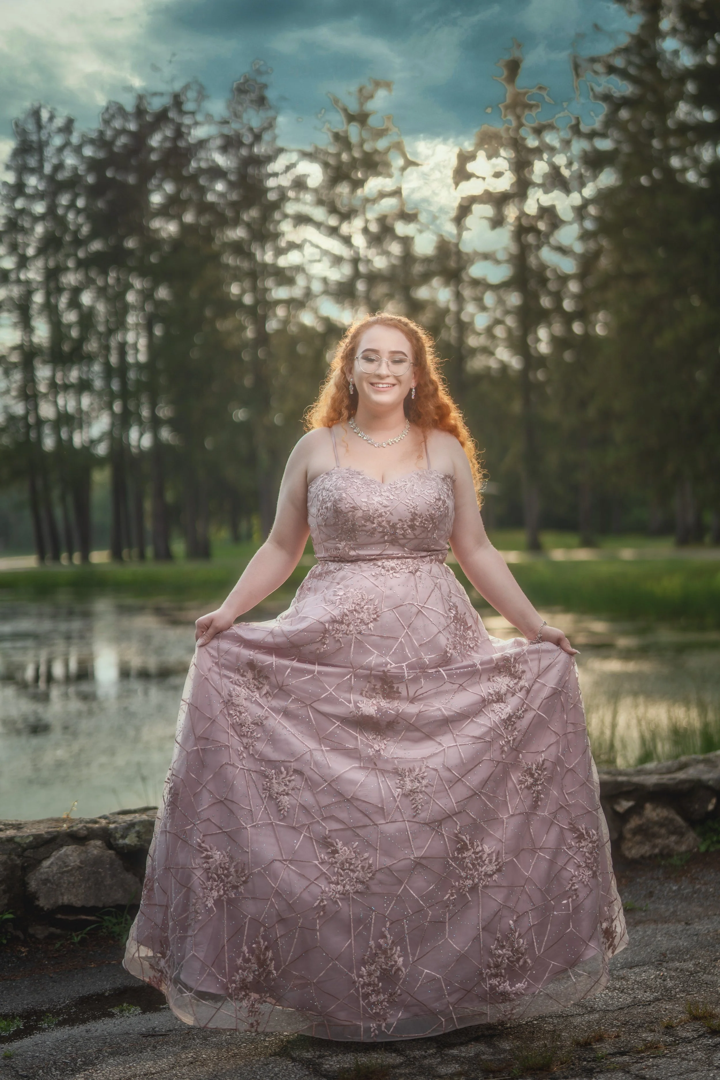 High school senior wearing a pink gown during an outdoor portrait session beside the water.