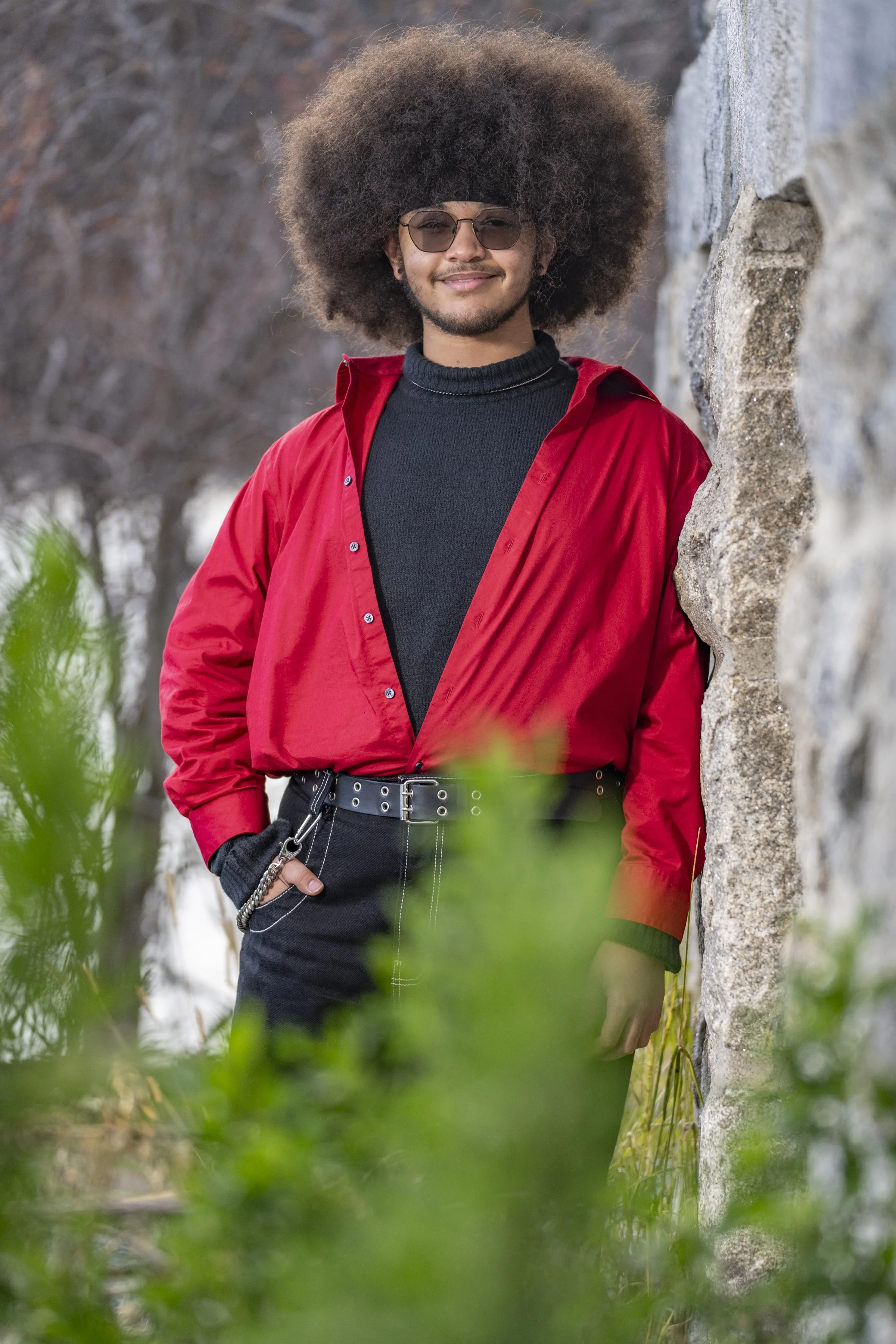 Stylish male high school senior in a red jacket photographed through green foliage