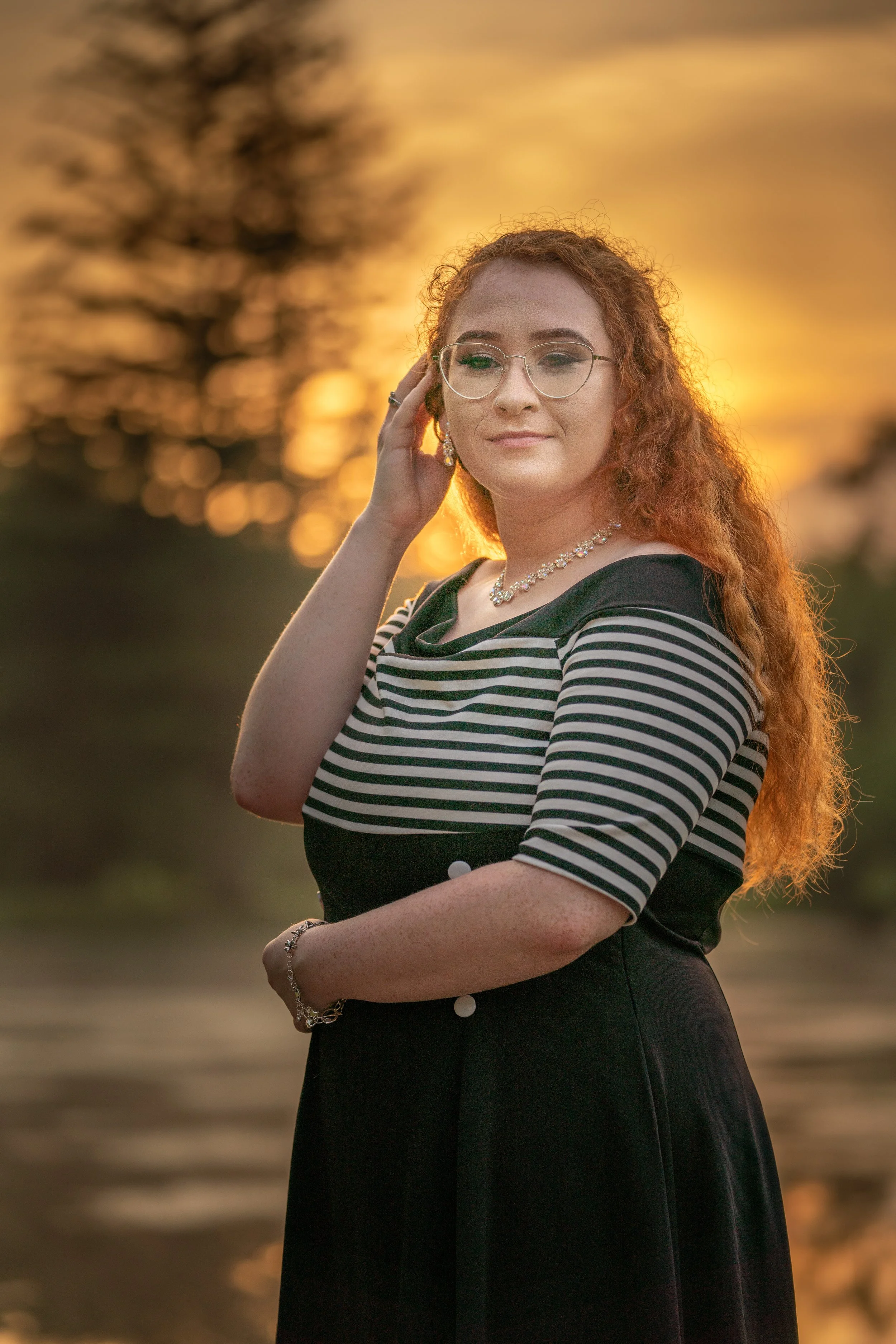 High school senior in a black striped outfit photographed in warm sunset light.