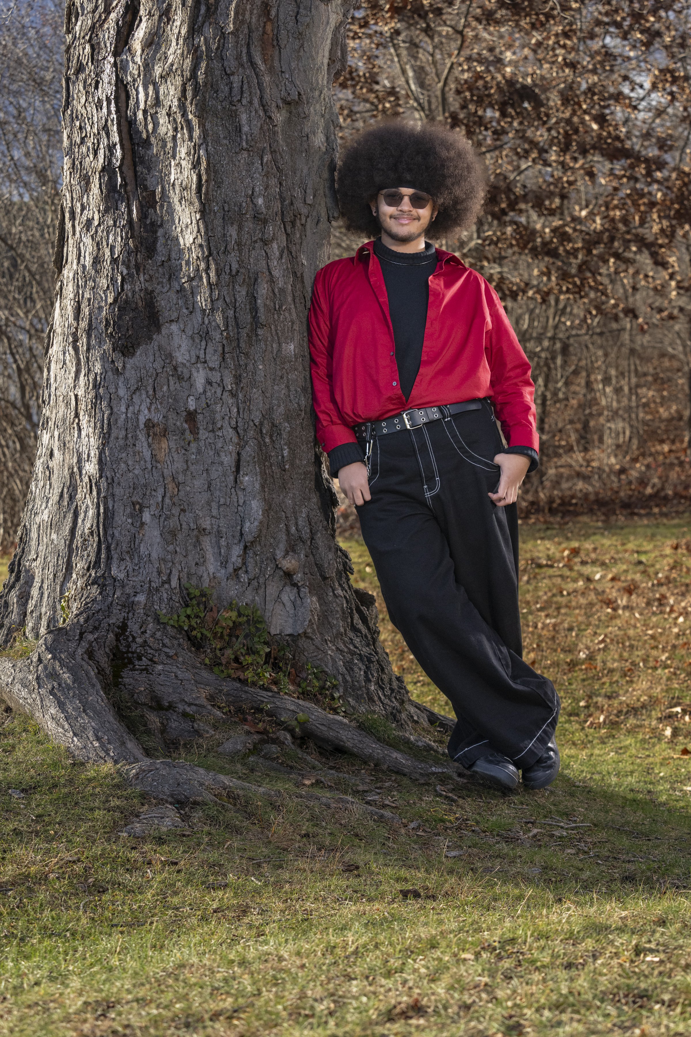 Male high school senior in a red jacket posing beside a large tree outdoors.