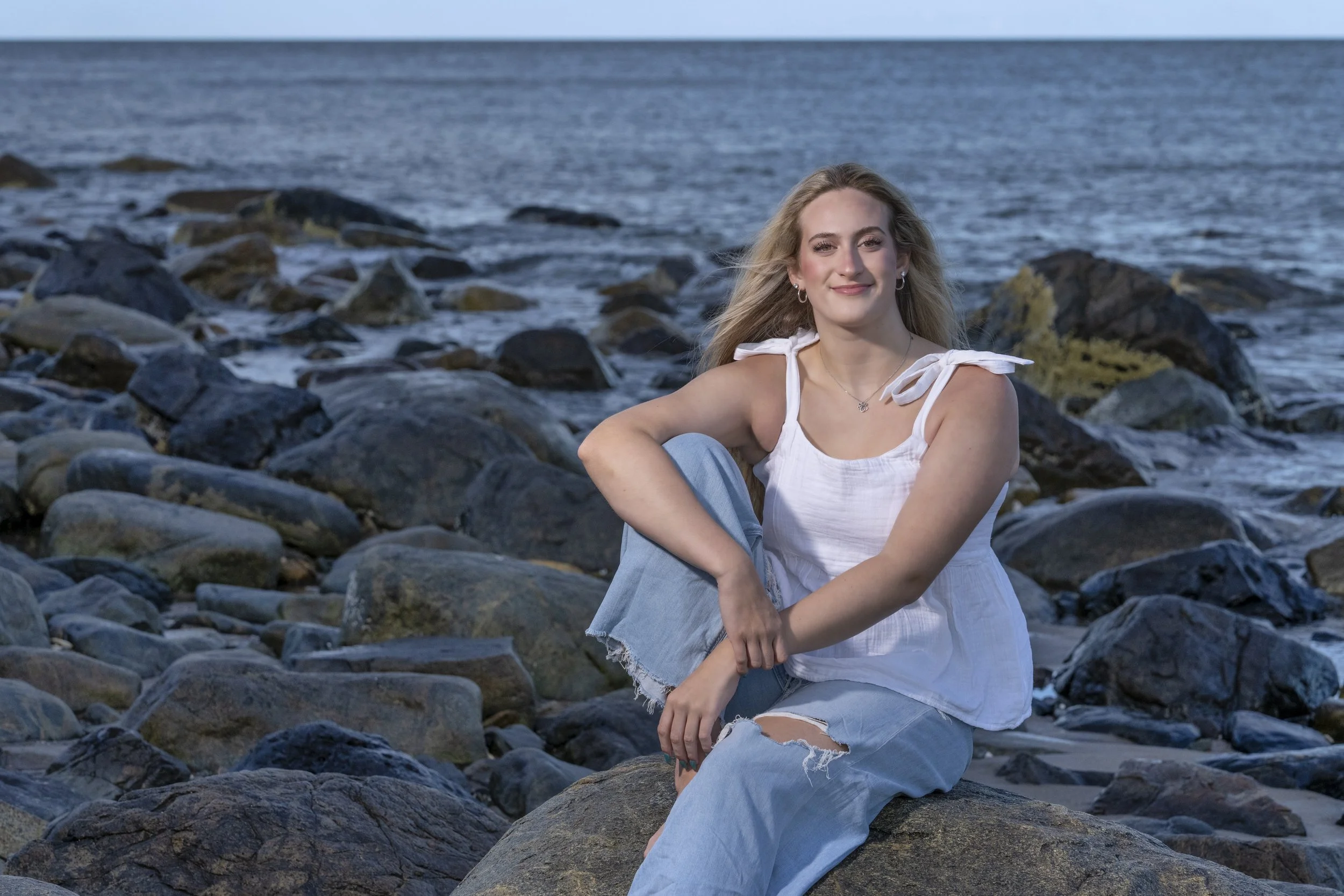 High school senior seated on coastal rocks during a New England beach session.