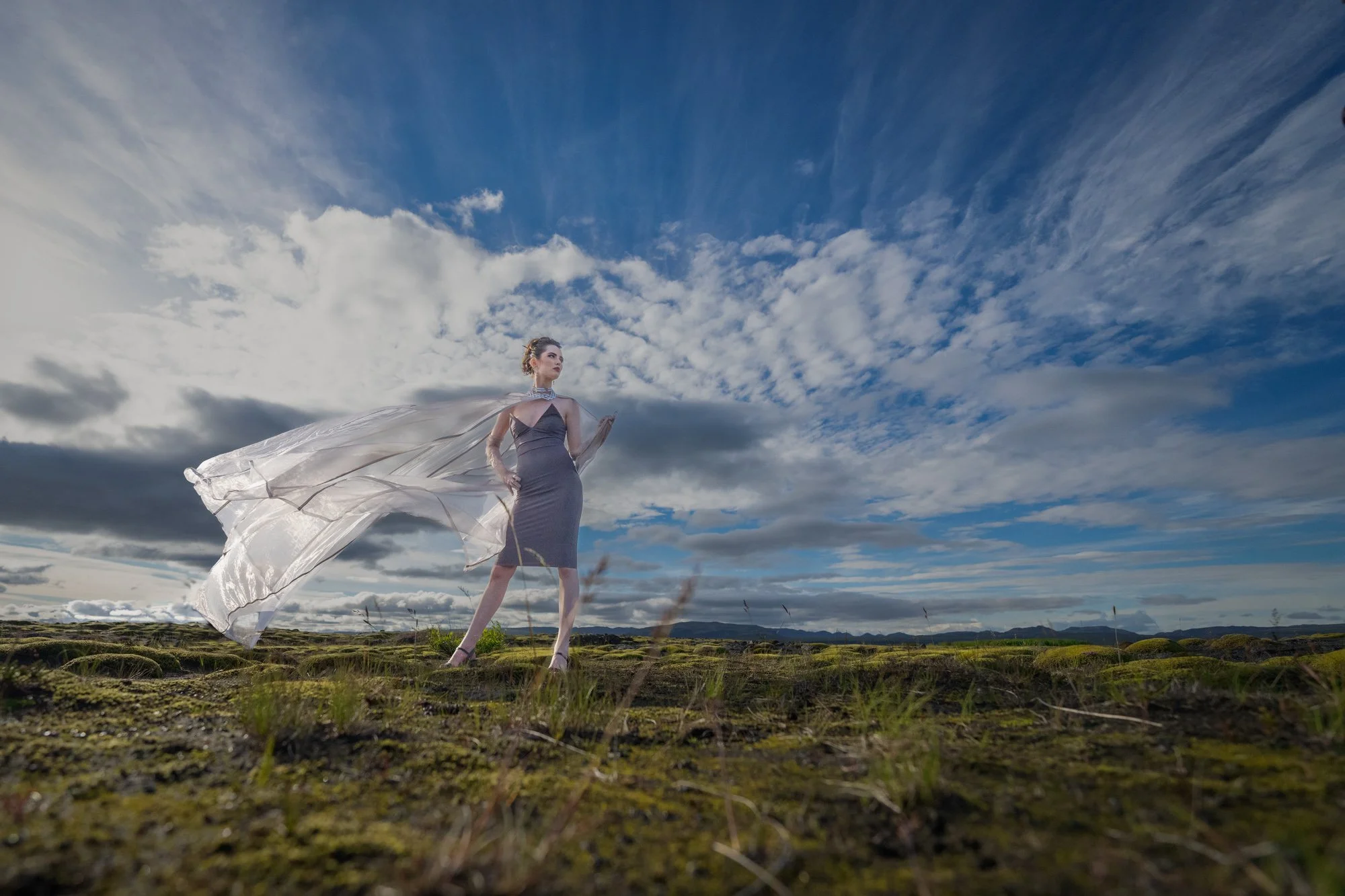 High school senior in a flowing white dress posing beneath a dramatic sky.