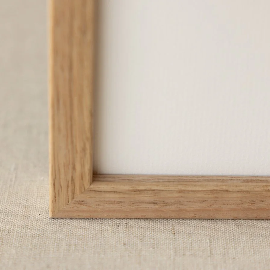 Close-up of a light wood picture frame corner on a beige fabric surface.