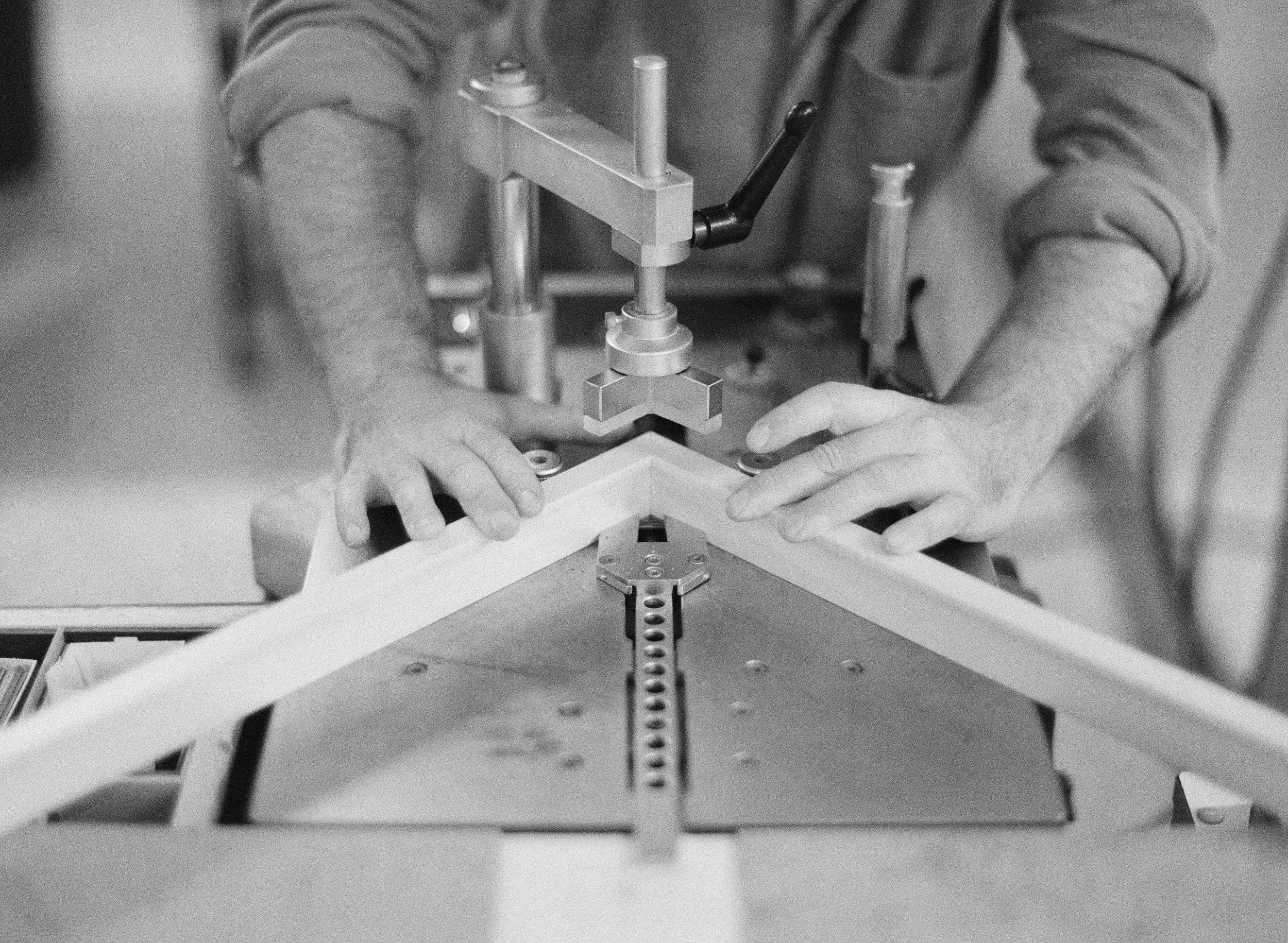 A person working with a precision machine on a white, angled object, with hands adjusting the object while operating the machine.