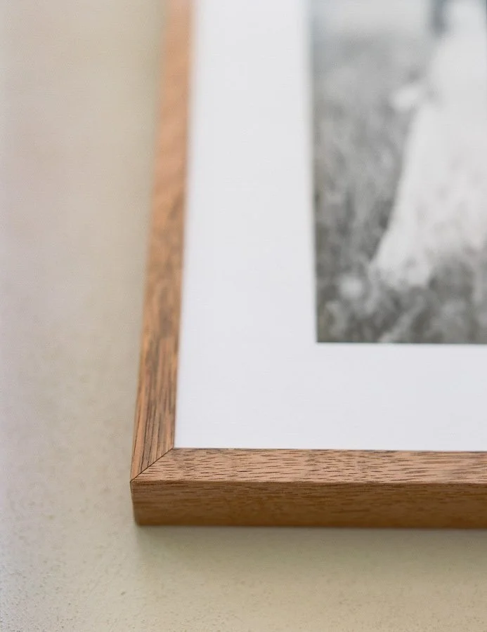 Close-up of a wooden picture frame with a white mat and black-and-white photo inside, resting on a beige surface.