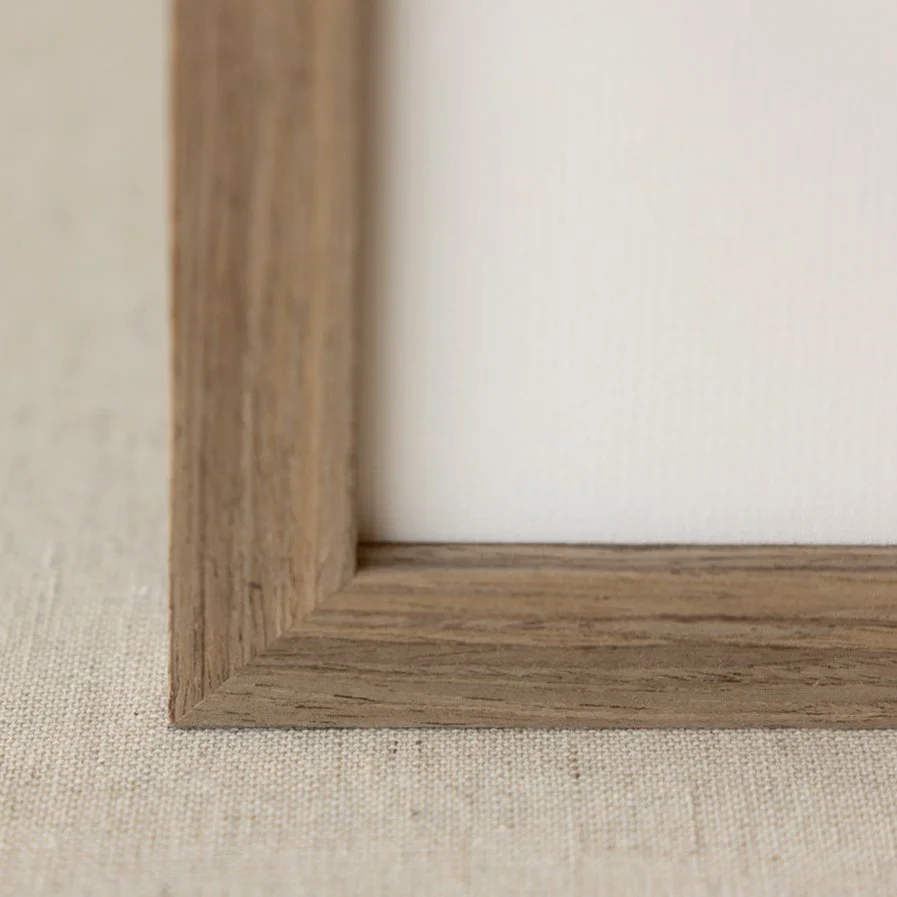 Close-up of a wooden picture frame corner placed on a beige fabric surface.