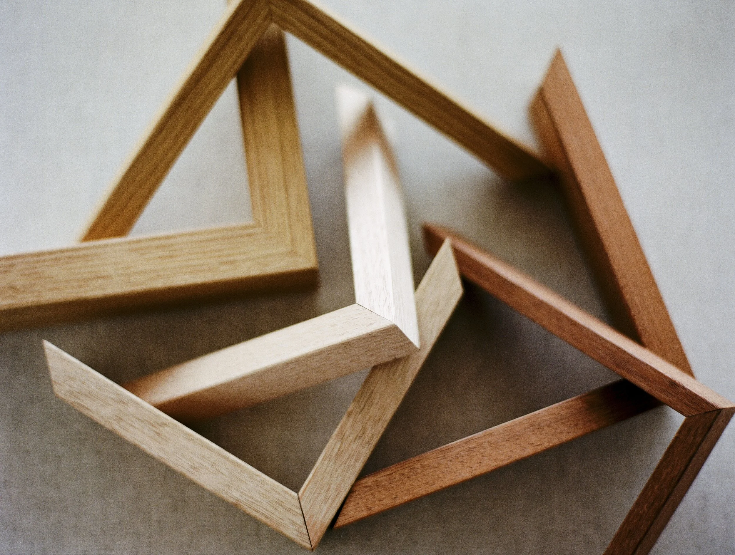 Three wooden geometric frames in different shades of brown and light wood lying on a grey surface.