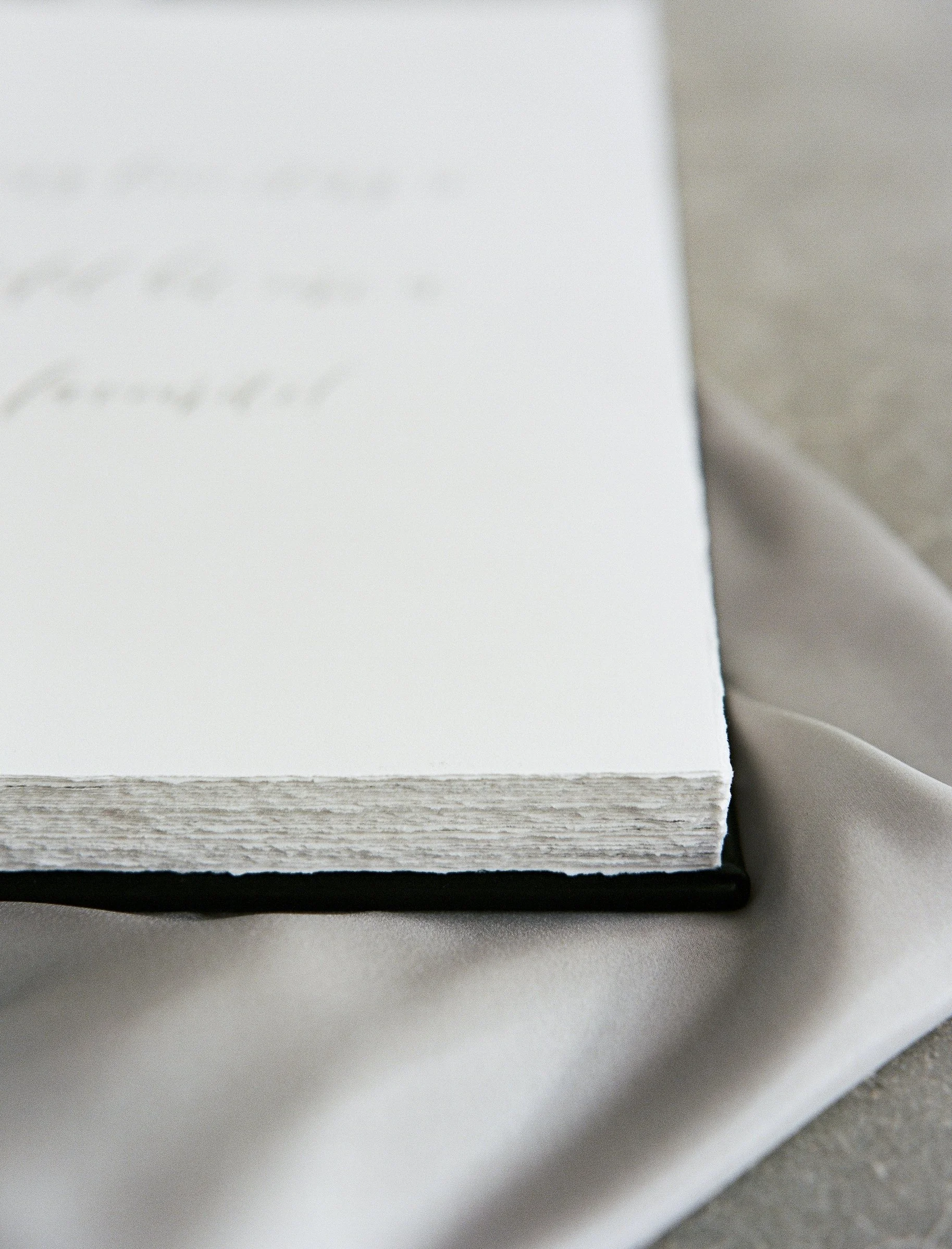Close-up of a white textured notebook or journal resting on a light gray fabric surface.