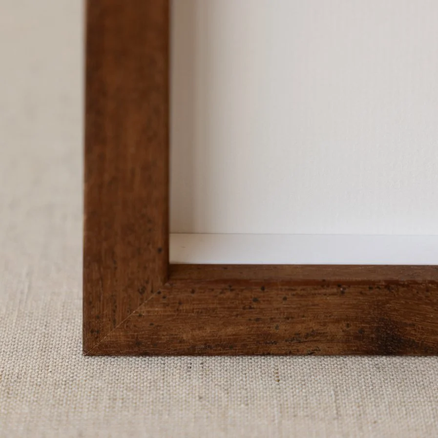 Close-up of a wooden picture frame corner on a beige textured surface.