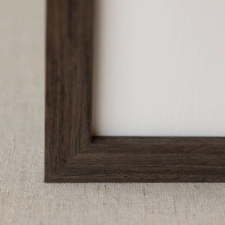 Close-up of a wooden picture frame corner on a light-colored fabric surface.