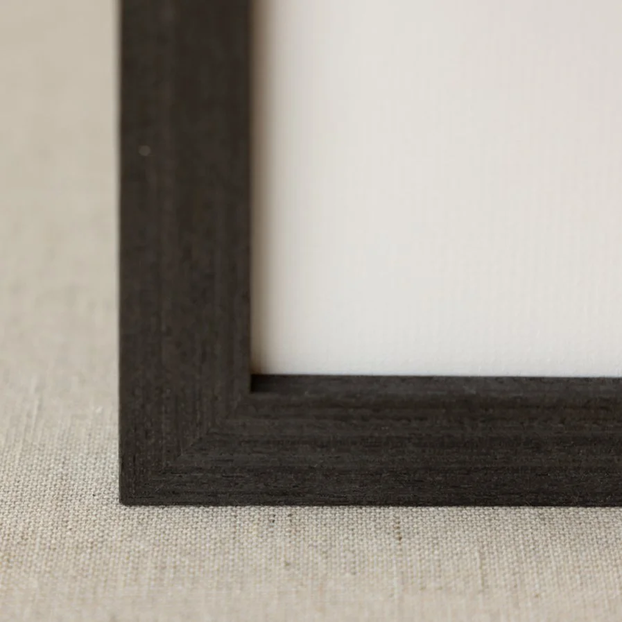 Close-up of a black picture frame with a white mat, resting on a textured beige surface.