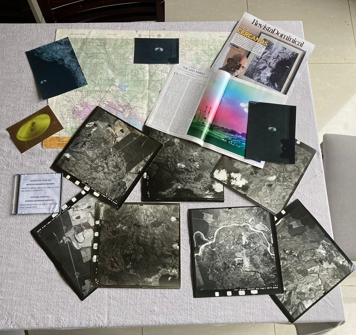 A table displaying various photos, maps, magazines, and documents related to UFOs and geography, including aerial photographs, a map of Costa Rica, and magazine articles.