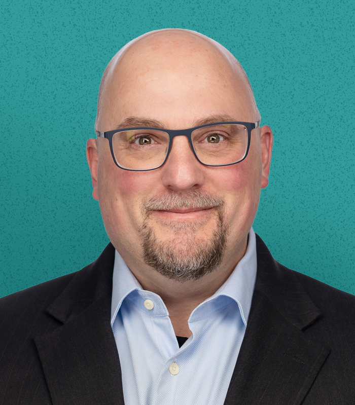 Headshot of David Fallace, a bald man with glasses smiling, dressed in a suit jacket and light blue shirt, with a teal textured background.