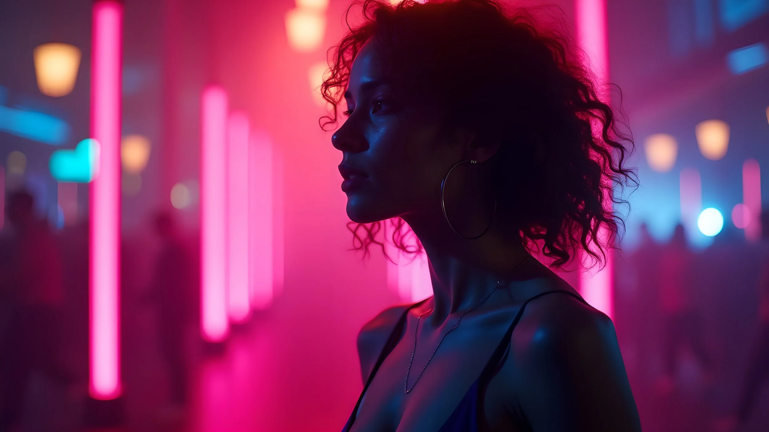 Side profile of a woman with curly hair in a neon-lit environment with pink and blue lights, wearing hoop earrings and a thin-strapped top.