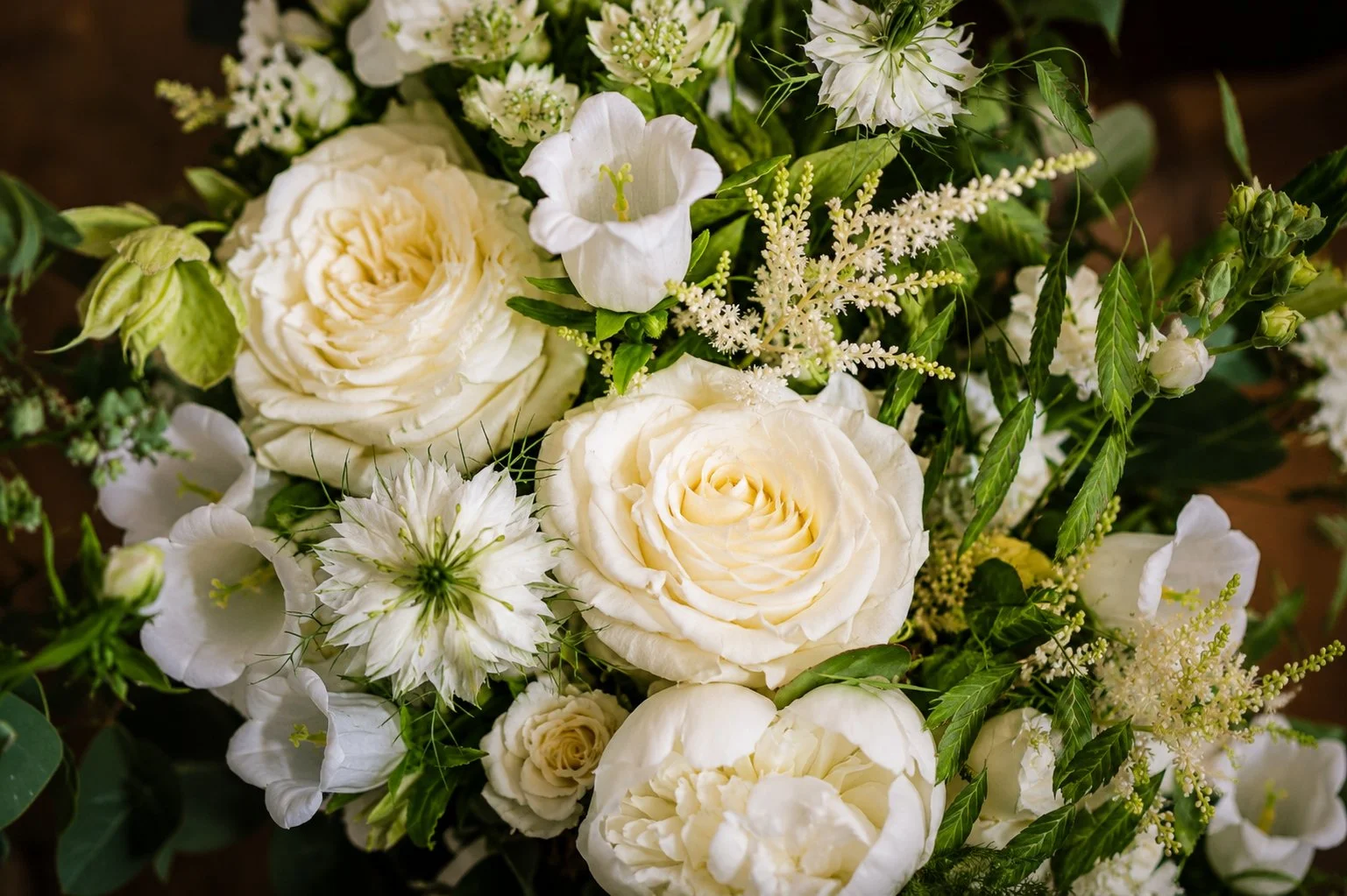 A close-up of a bouquet with white roses, white lilies, and various white and green flowers and foliage.
