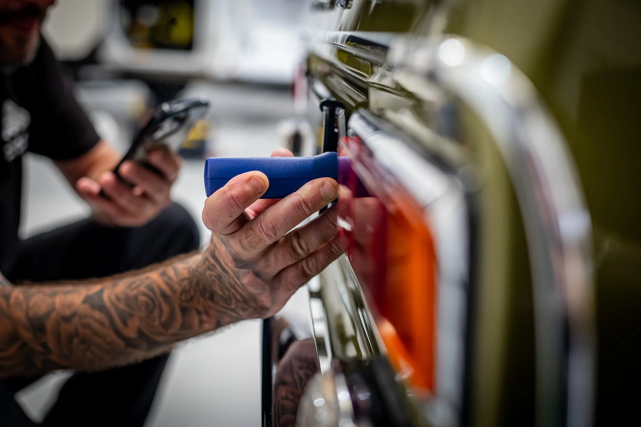 Person with tattooed arm holding a blue item while working on a vehicle's door.