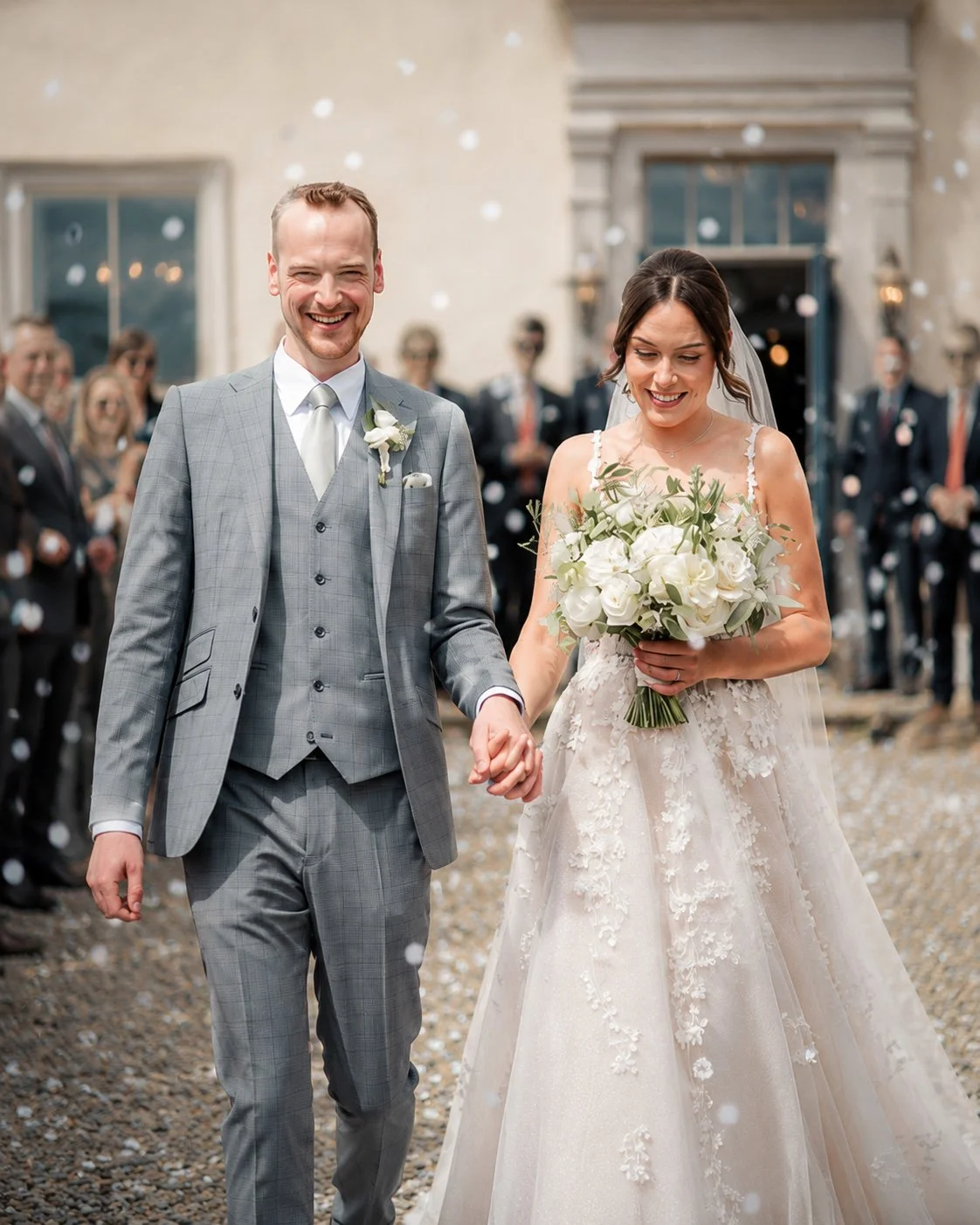 A newlywed couple walking after their wedding ceremony, surrounded by friends and family, with falling confetti in the background.