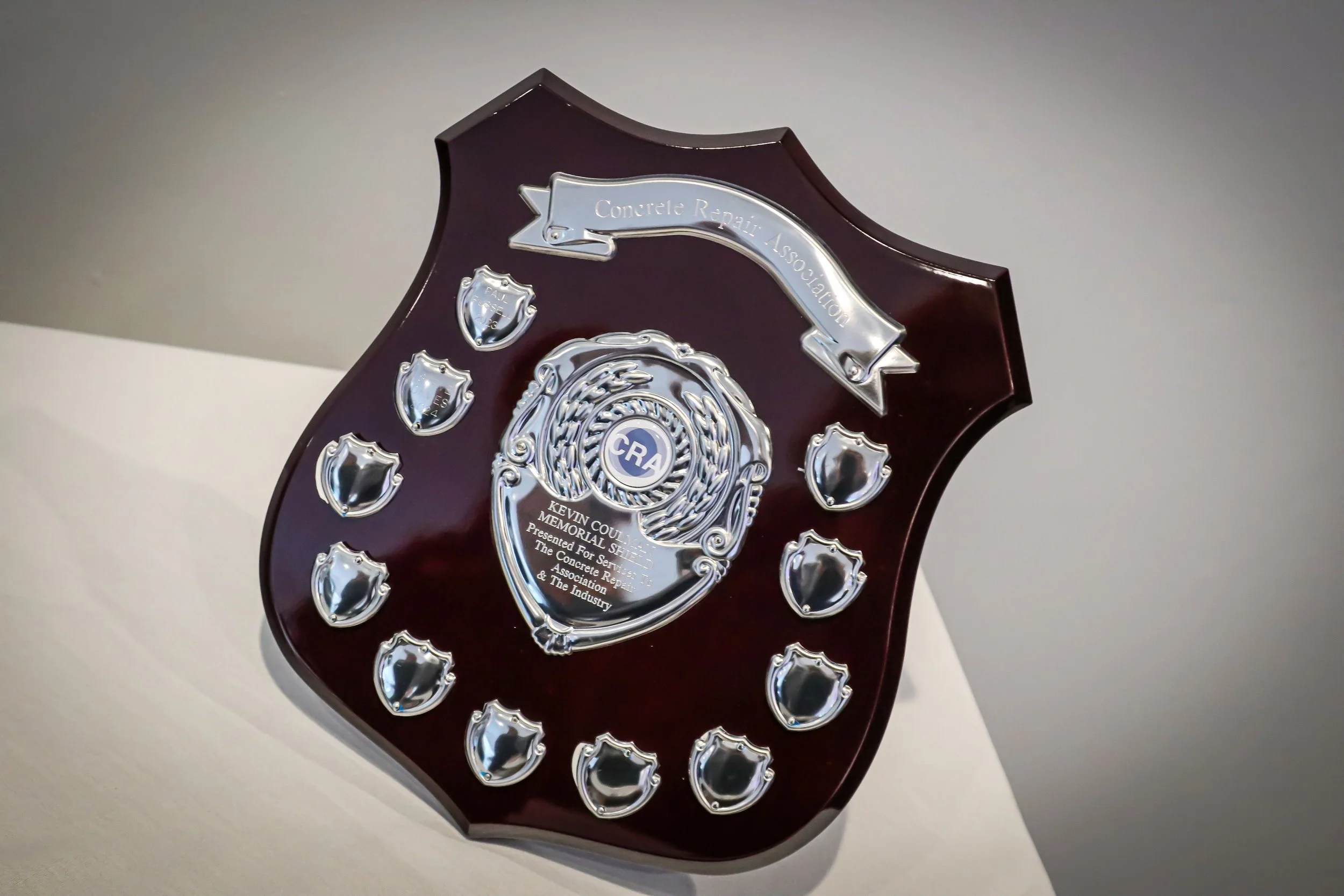 A wooden plaque with silver metal accents and shields, inscribed with the text: 'Concrete Repair Association.'