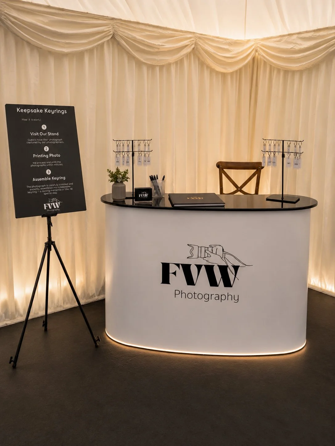 Event registration desk for FW Photography with keyrings and flowers, set against creamy draped backdrop.
