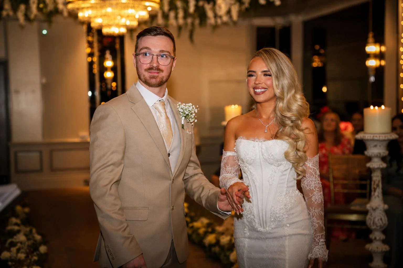 A bride and groom holding hands during their wedding ceremony in a decorated indoor venue.