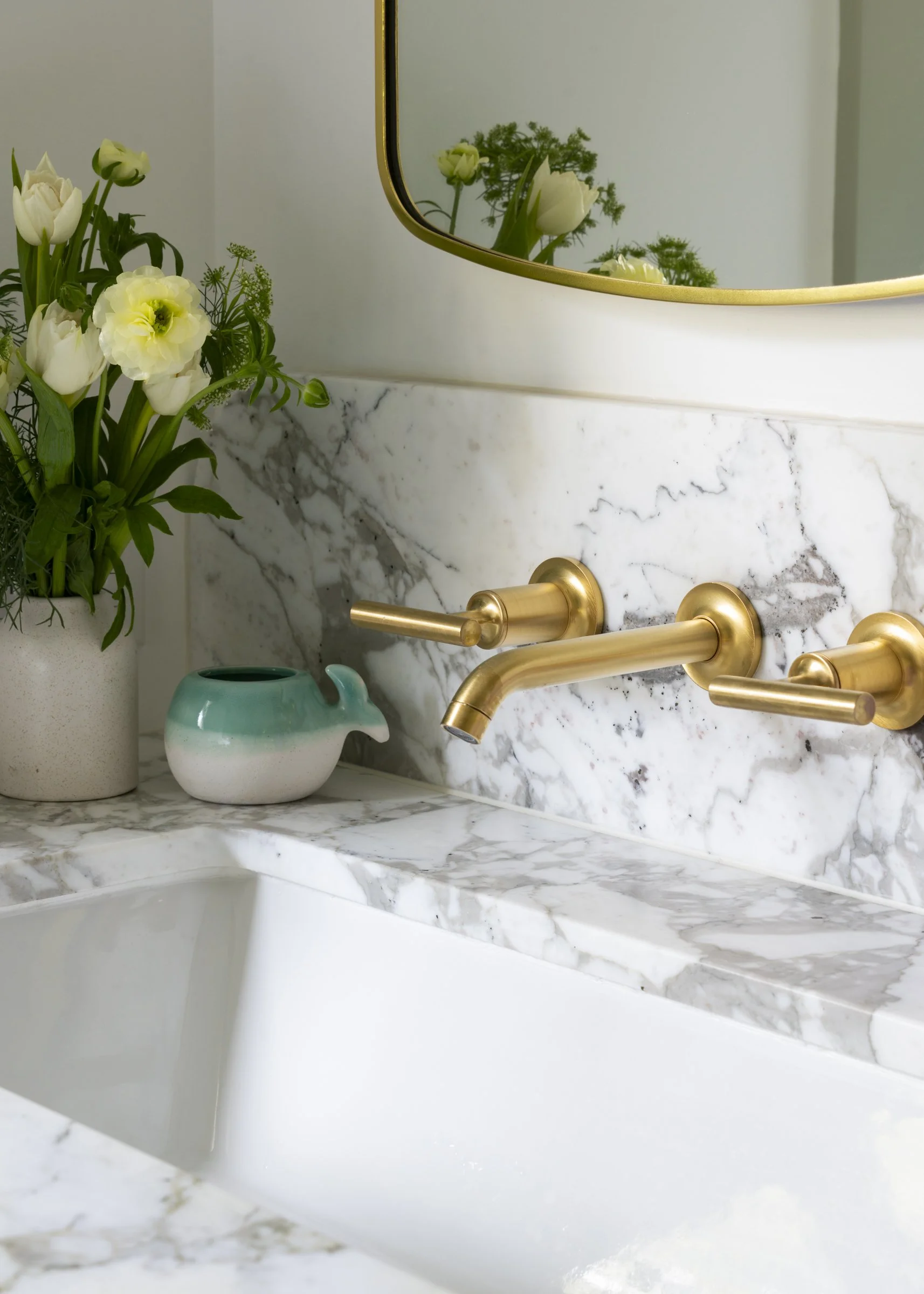 Marble bathroom countertop with a built-in sink, gold faucet, a potted flower arrangement, and a small ceramic duck-shaped object.