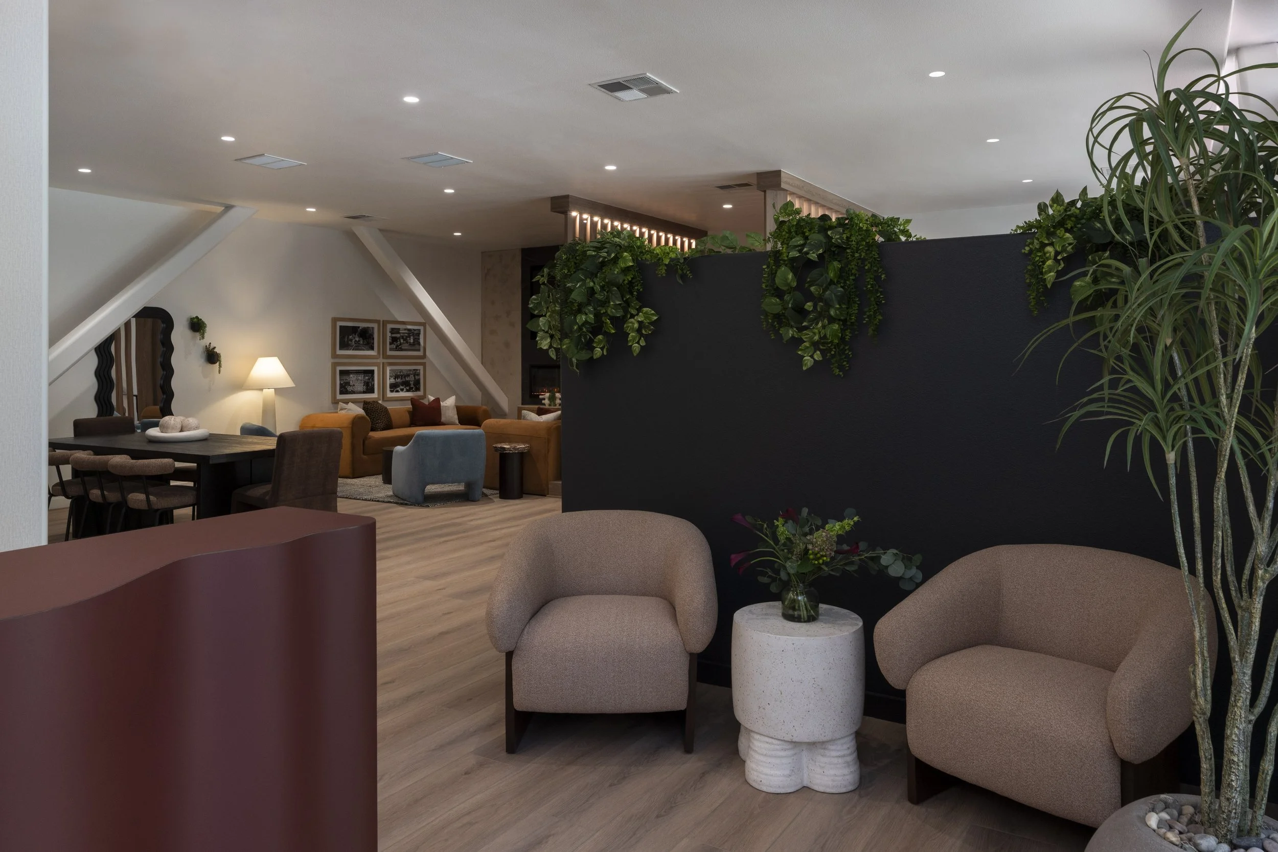 Modern hotel lobby with seating area, green plants, black wall, and gray chairs