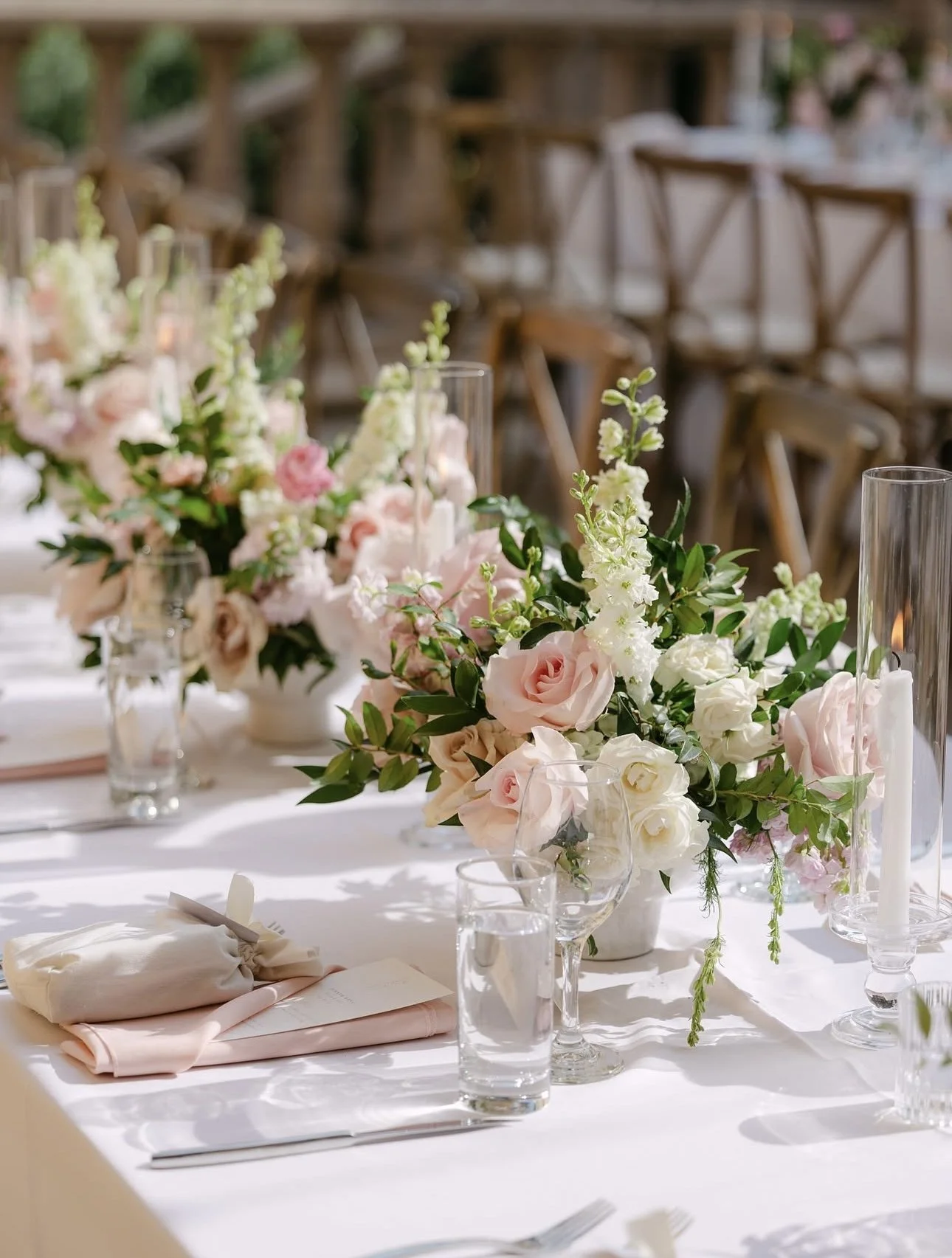 Elegant table setting with floral centerpieces, candles, glasses, and napkins in a bright dining area.