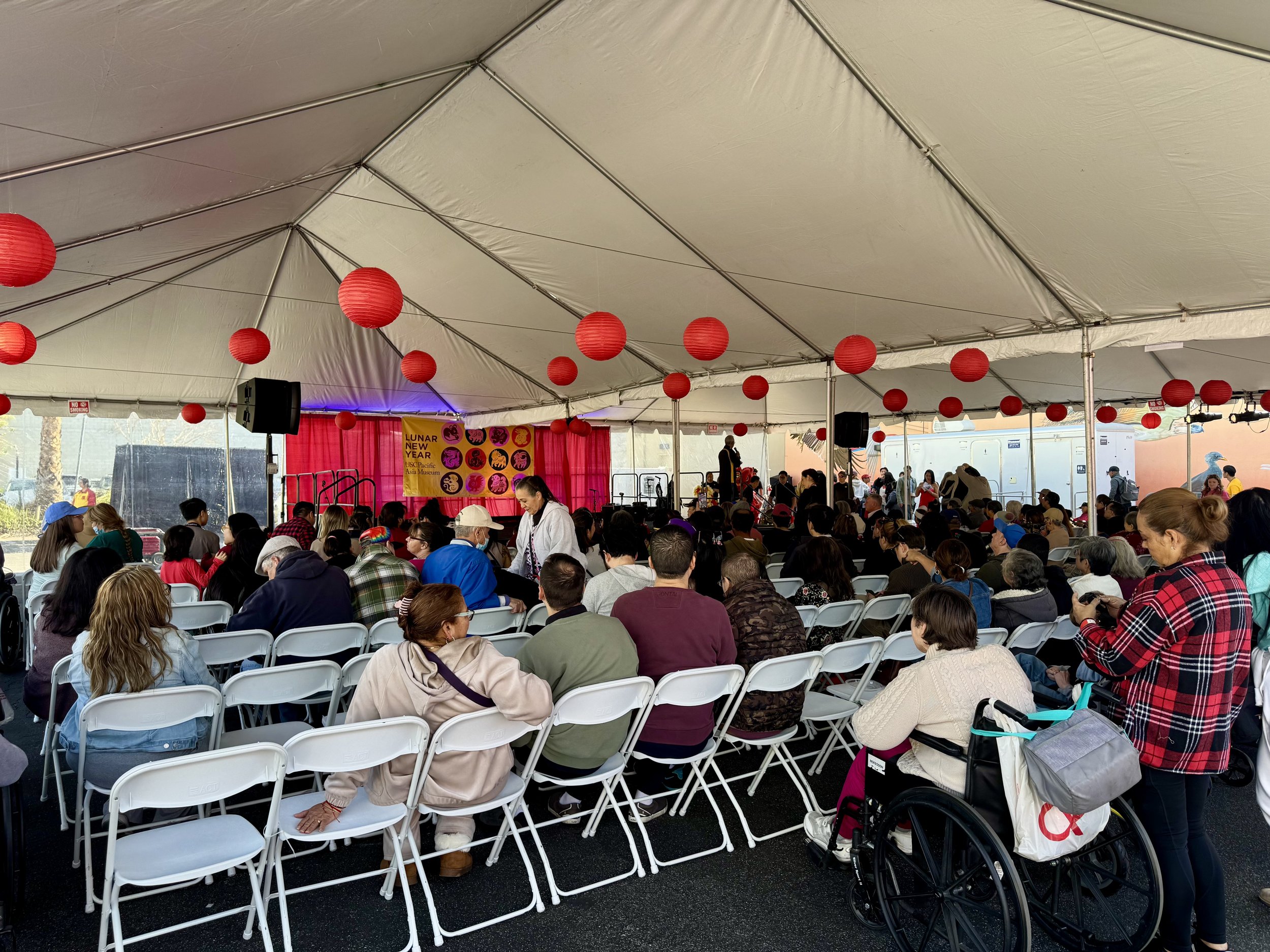Large tent event with people seated, red lanterns, and a Lunar New Year stage setup.