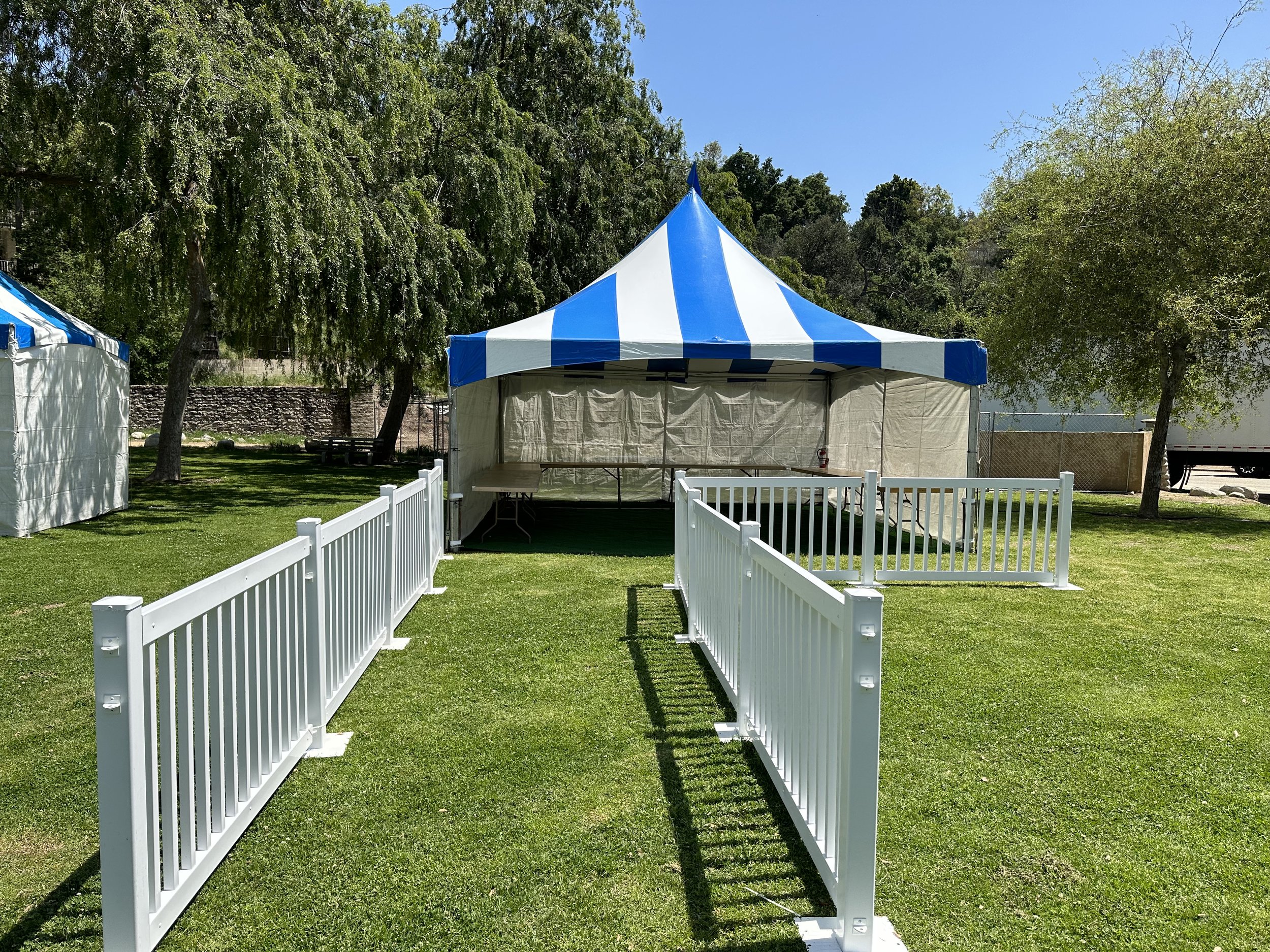 Blue and white striped tent with white fencing in a grassy outdoor area.