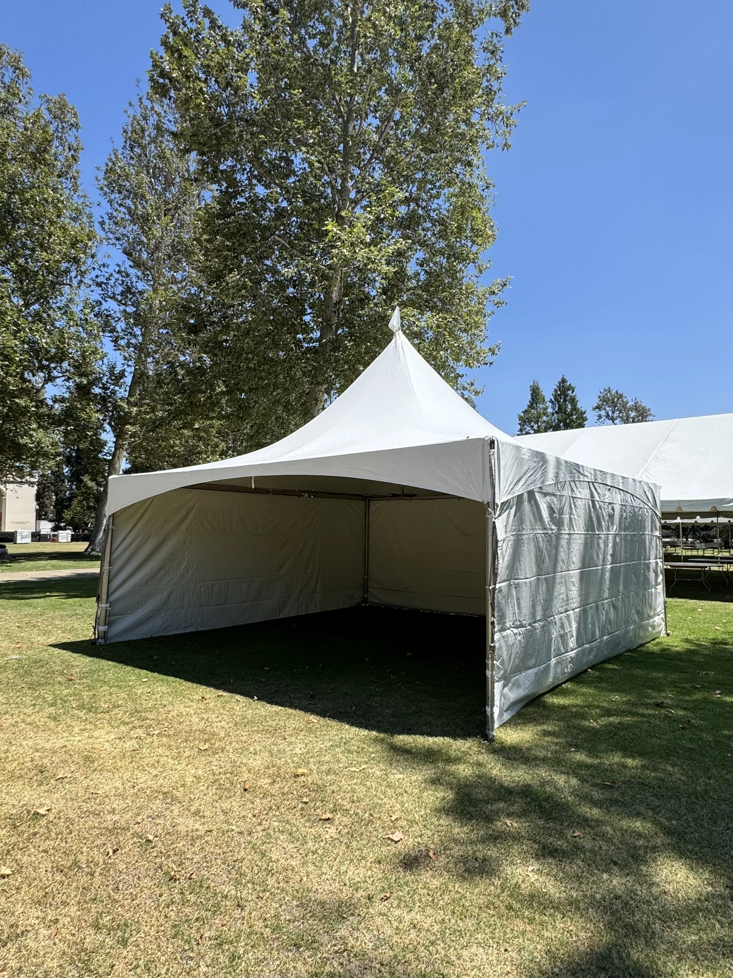 A large white event tent set up on a grassy area with trees and a blue sky in the background.