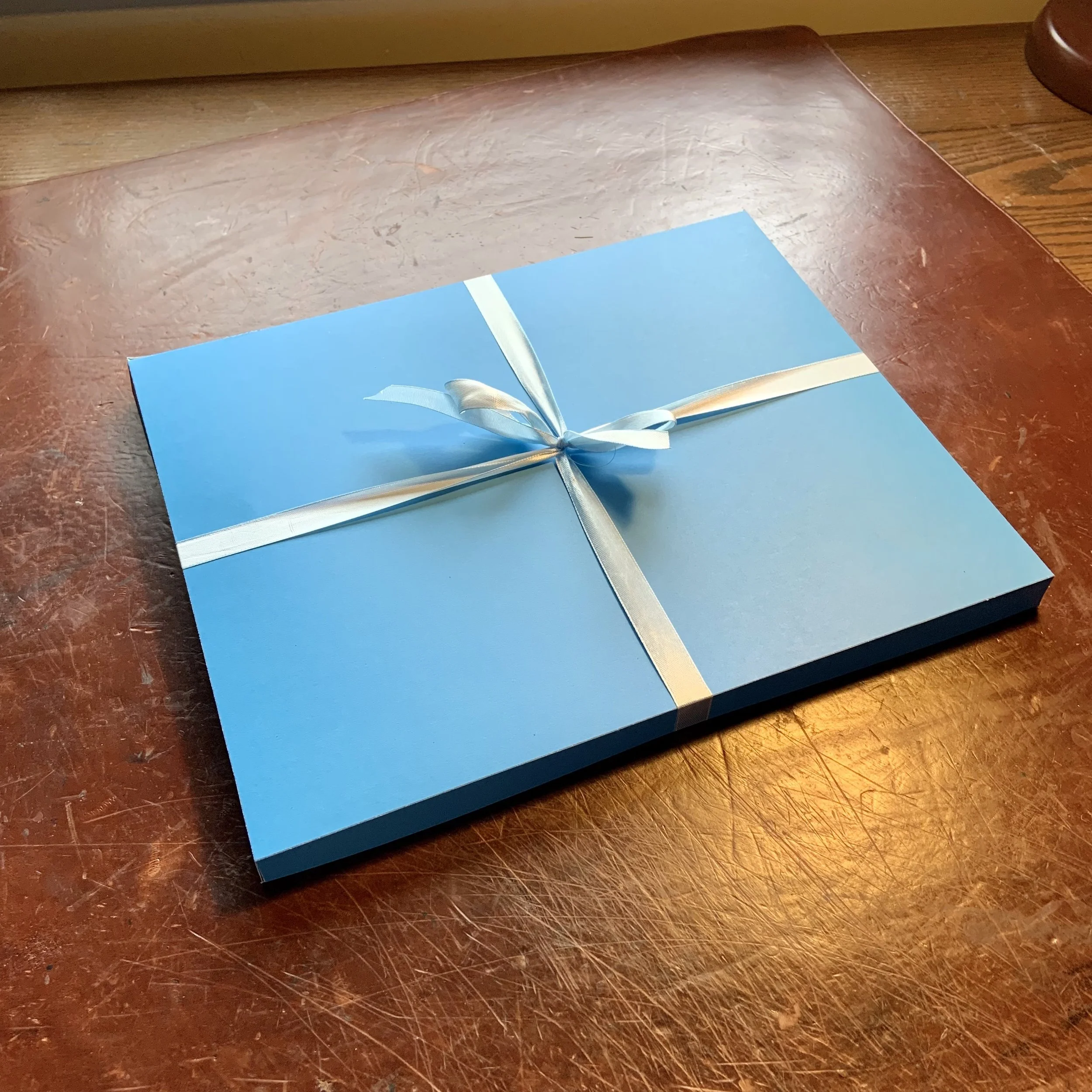 A blue gift box with a cream-colored ribbon placed on a wooden table.