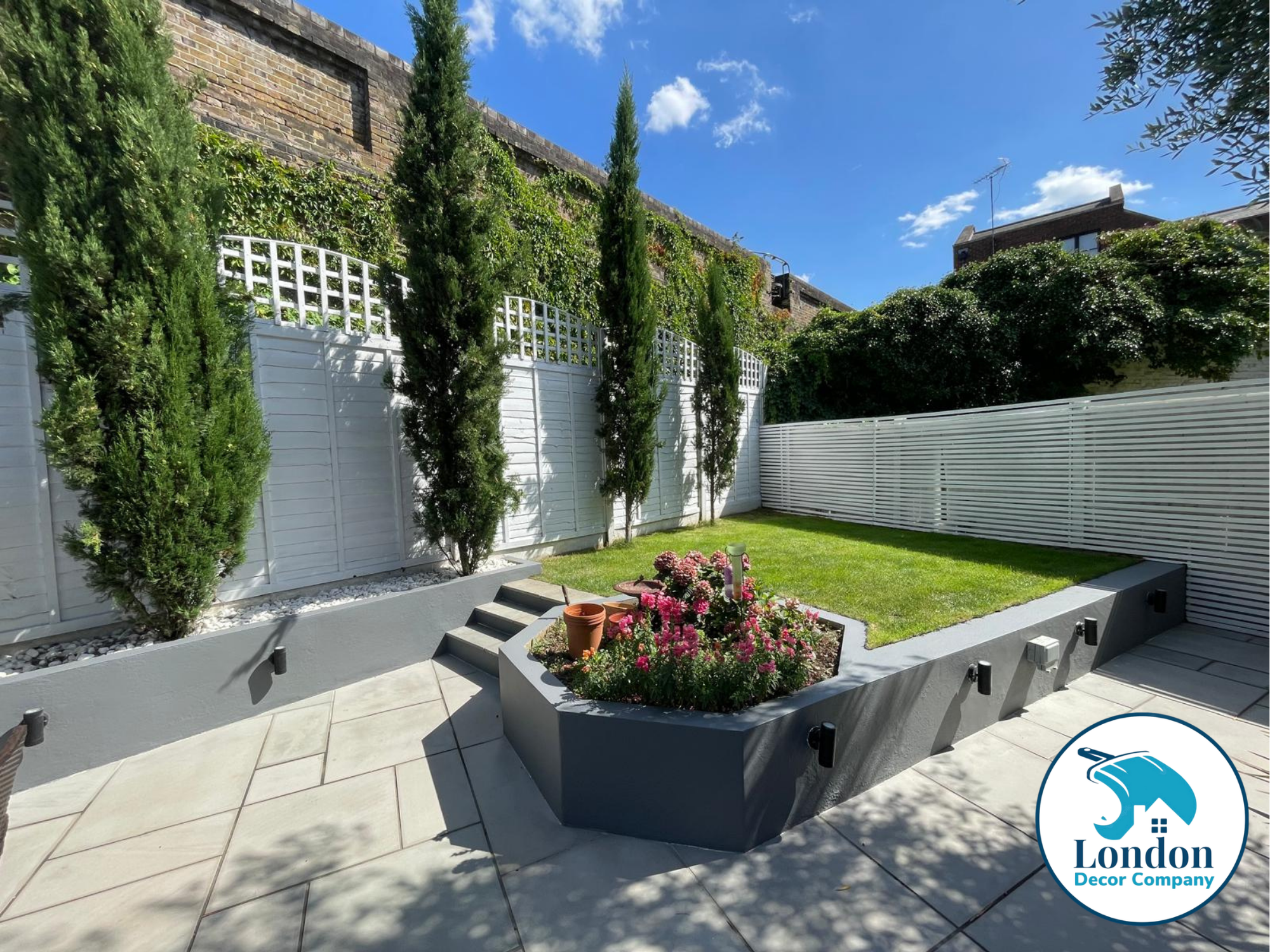 Garden patio with grey Dulux Weathershield masonry walls and freshly painted white fence panels, lawn and raised flower bed.