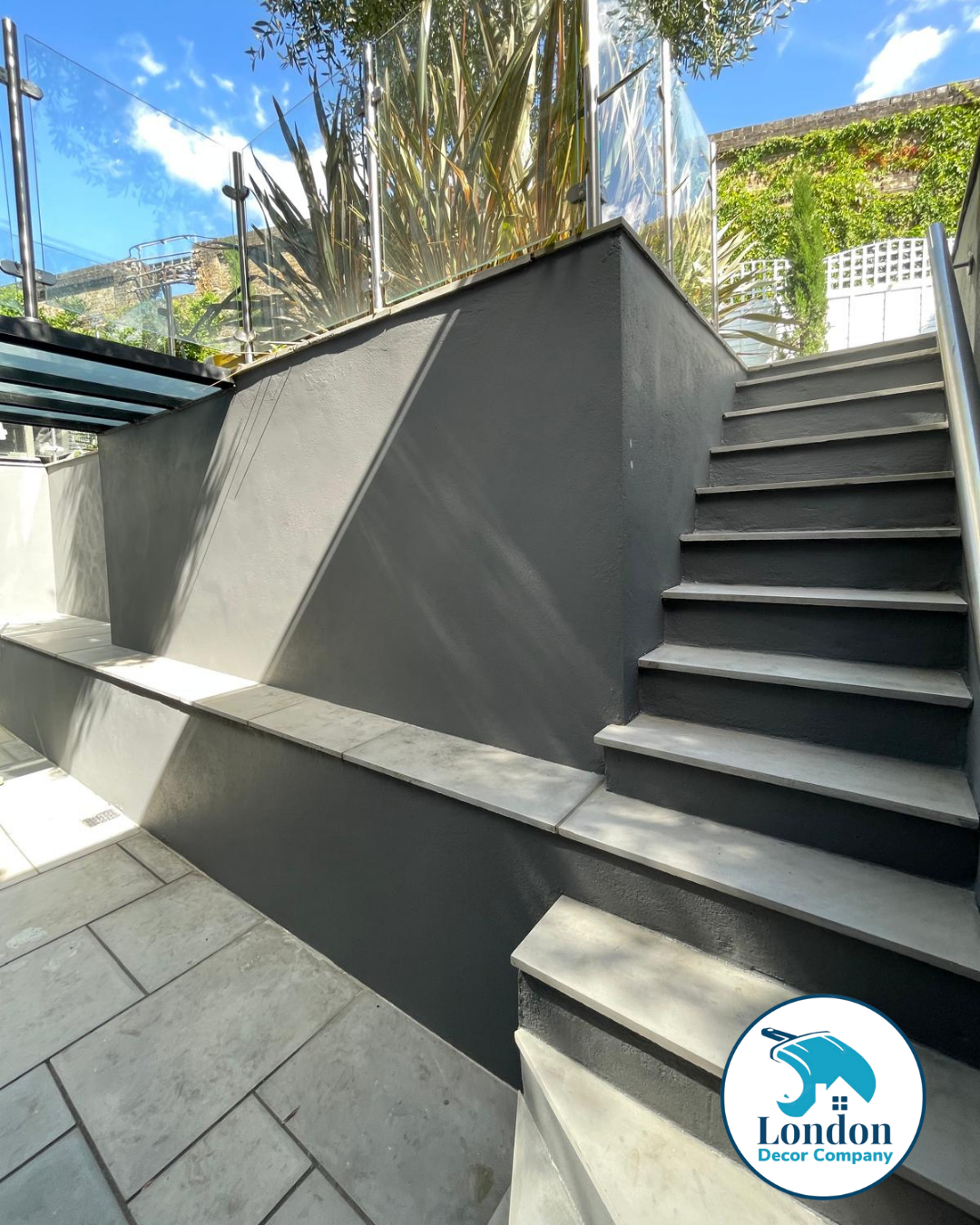 Close-up of grey rendered steps and retaining wall finished in Dulux Weathershield, with white painted fence panels behind.