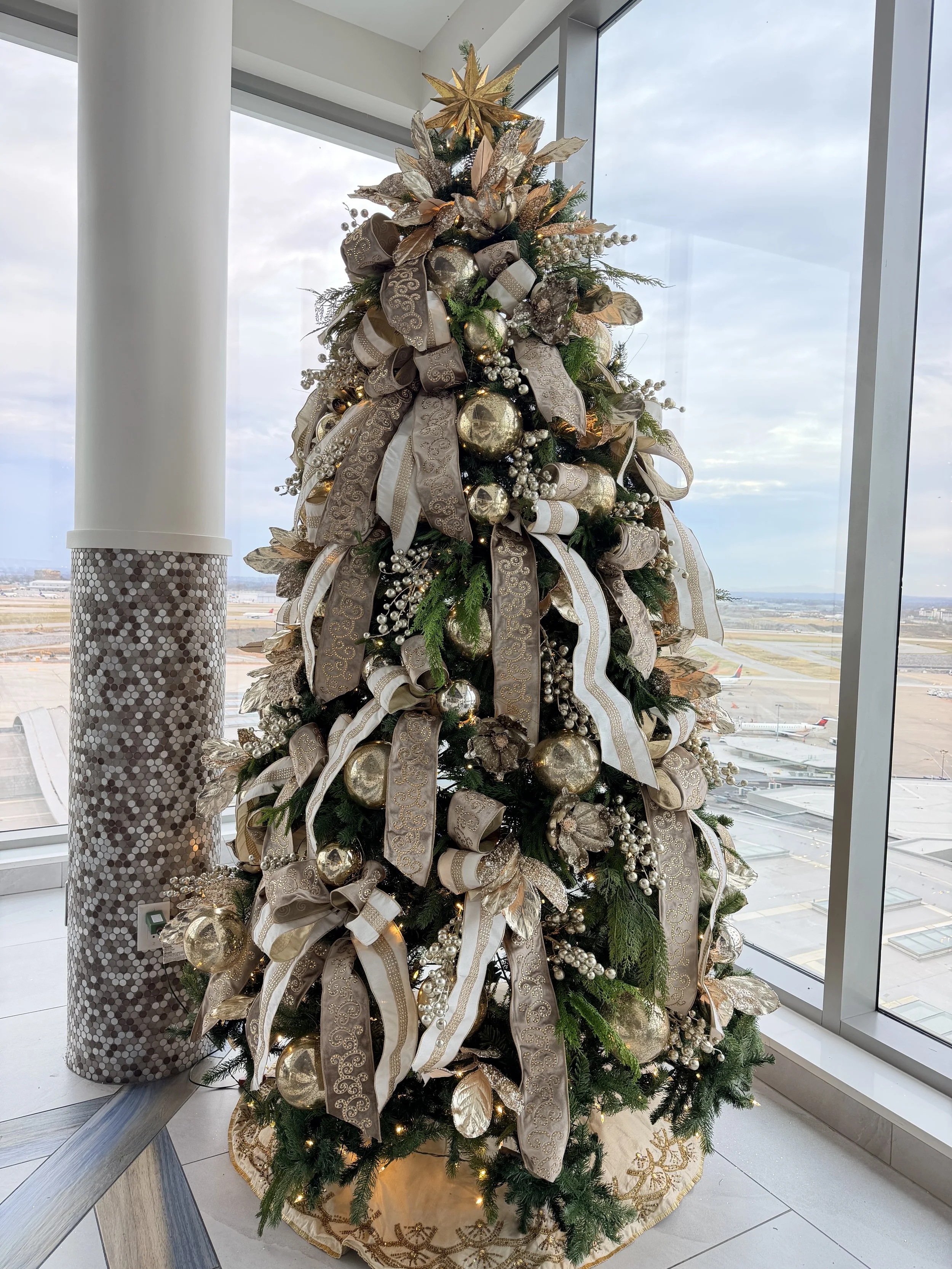 Luxury Christmas tree in the Hilton BNA Nashville Airport lobby designed by Whitney Elaine Interiors featuring champagne ribbon, metallic ornaments, and elegant holiday décor.