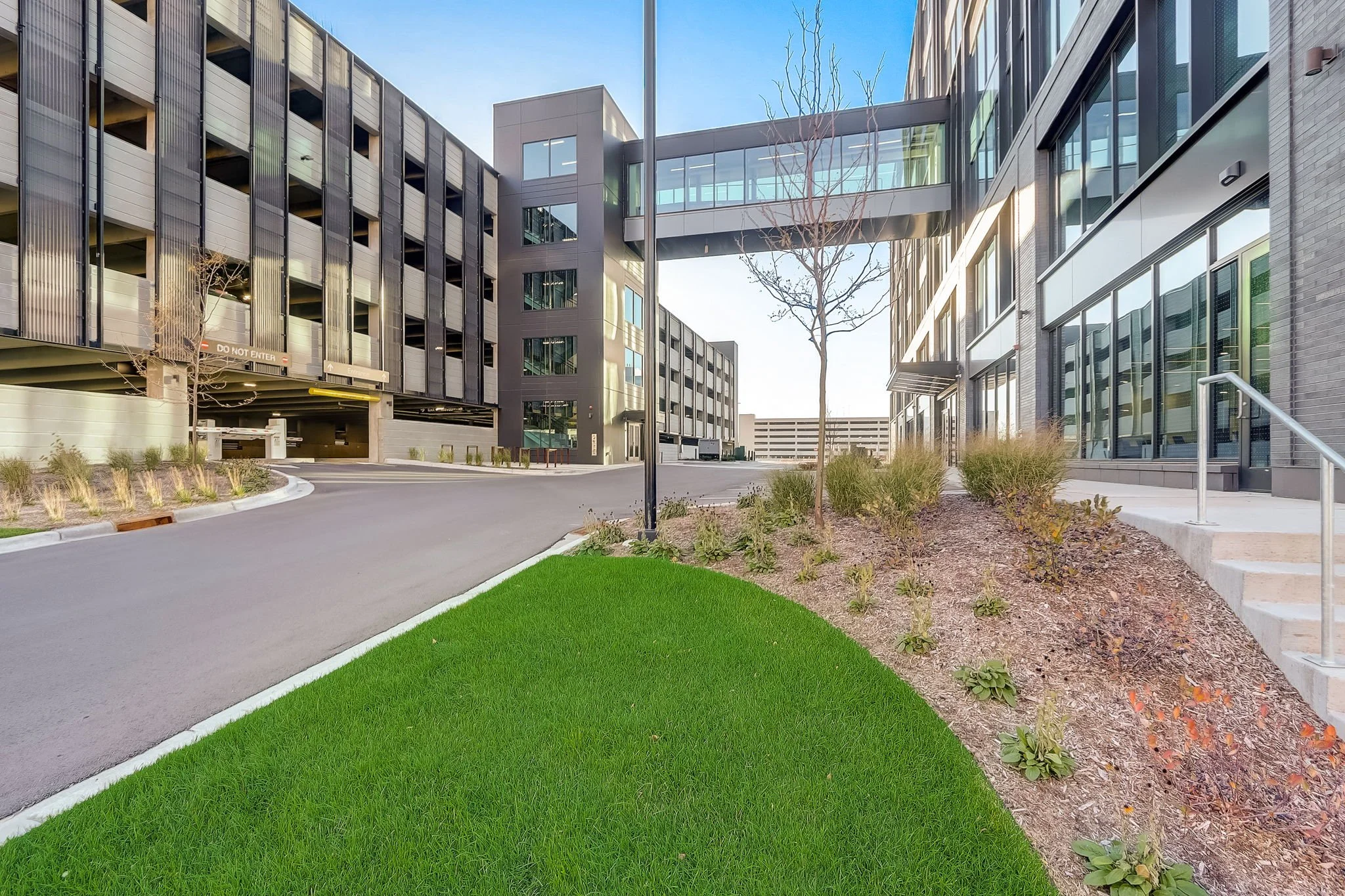 Modern office building with glass walkway, landscaped garden, and parking structure