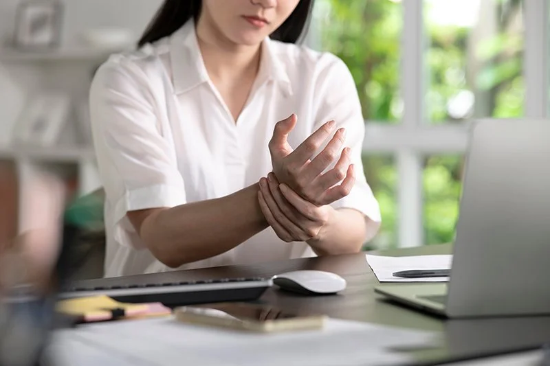 Woman holding her wrist due to pain while sitting at a desk