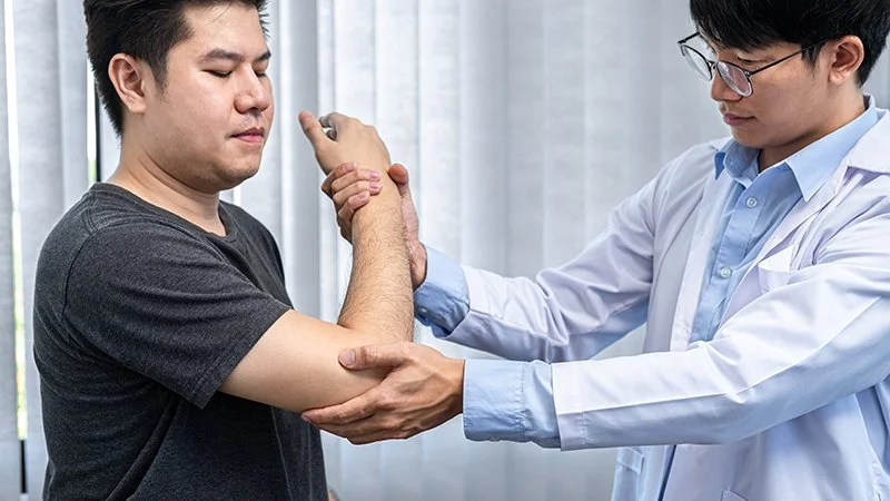 Physiotherapist assessing elbow movement and discomfort during a clinical examination