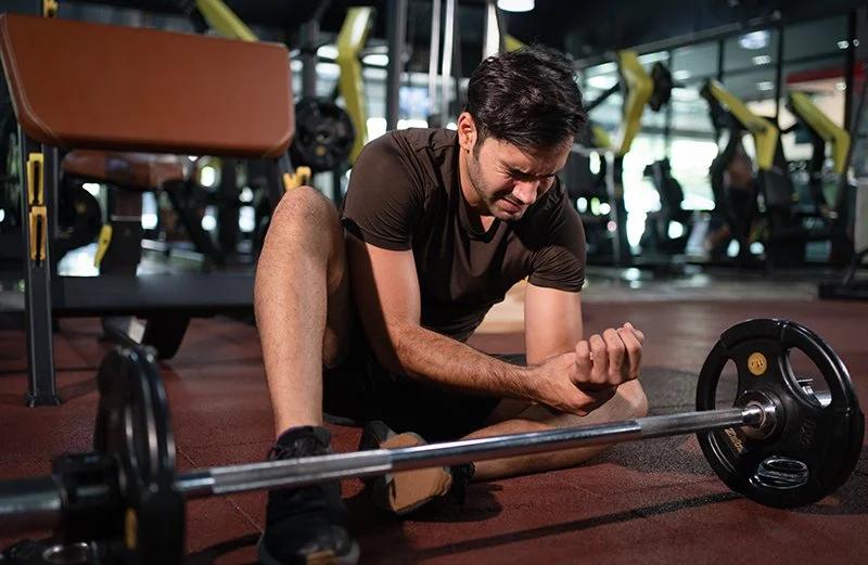 Man sitting in a gym holding his wrist after experiencing pain during weightlifting