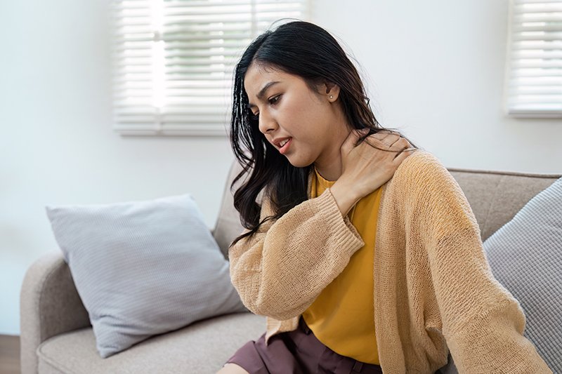 Woman sitting at home holding her shoulder due to neck and shoulder pain