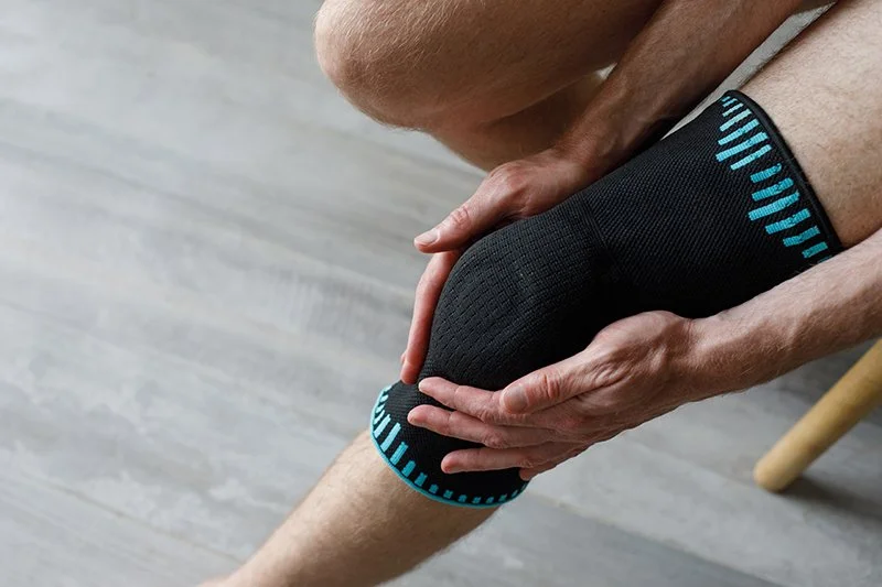 Person supporting their knee while wearing a brace during post surgery rehabilitation