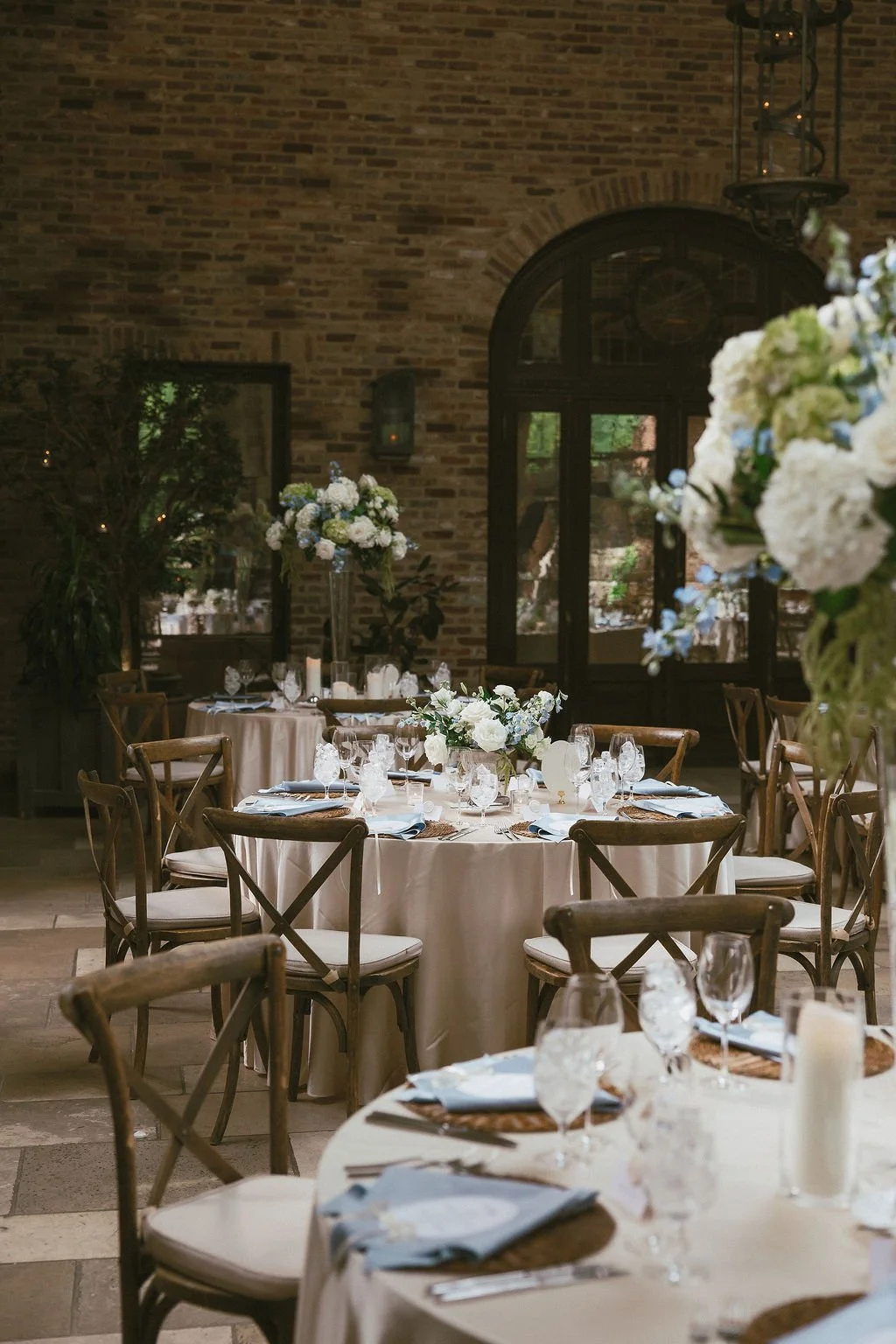 Elegant banquet hall with round tables draped in white tablecloths, decorated with floral centerpieces and fine glassware, set for a formal event.