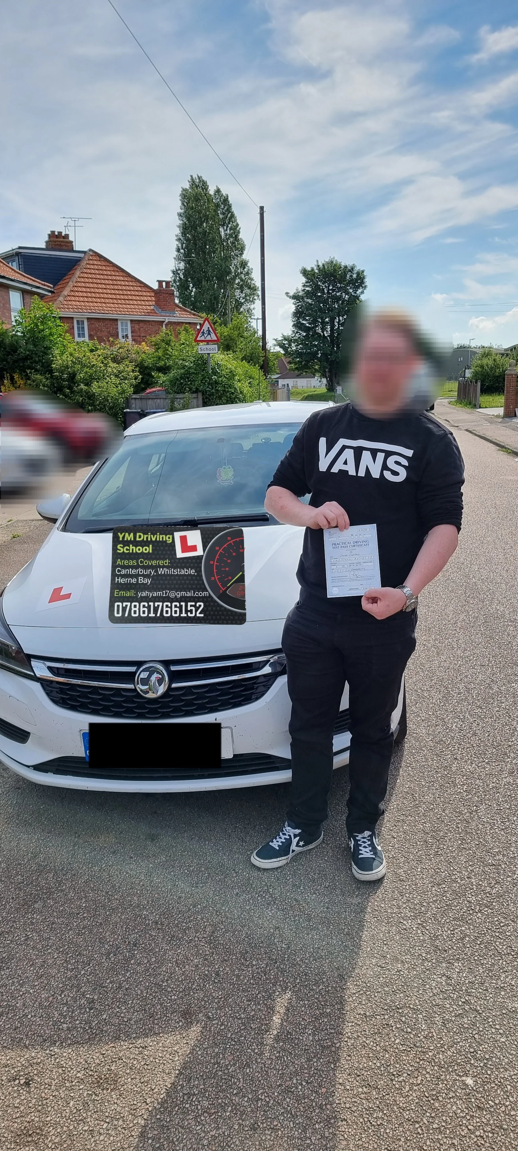 A person standing in front of a white car holding a paper, with a sign on the car advertising a driving school, and a blurred car driving by in the background.