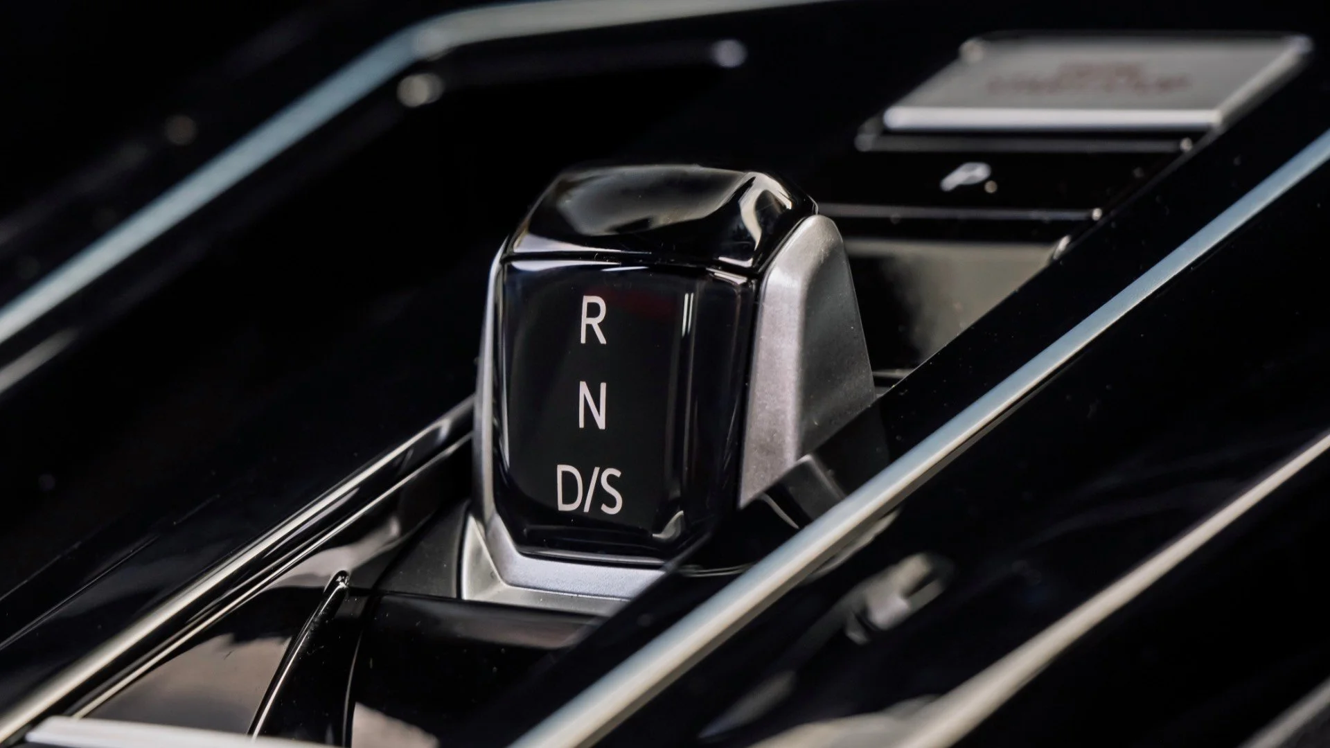 Close-up view of a modern car gear shifter with labels R, N, D, S, and plus/minus symbols for gear selection, on a shiny black surface.