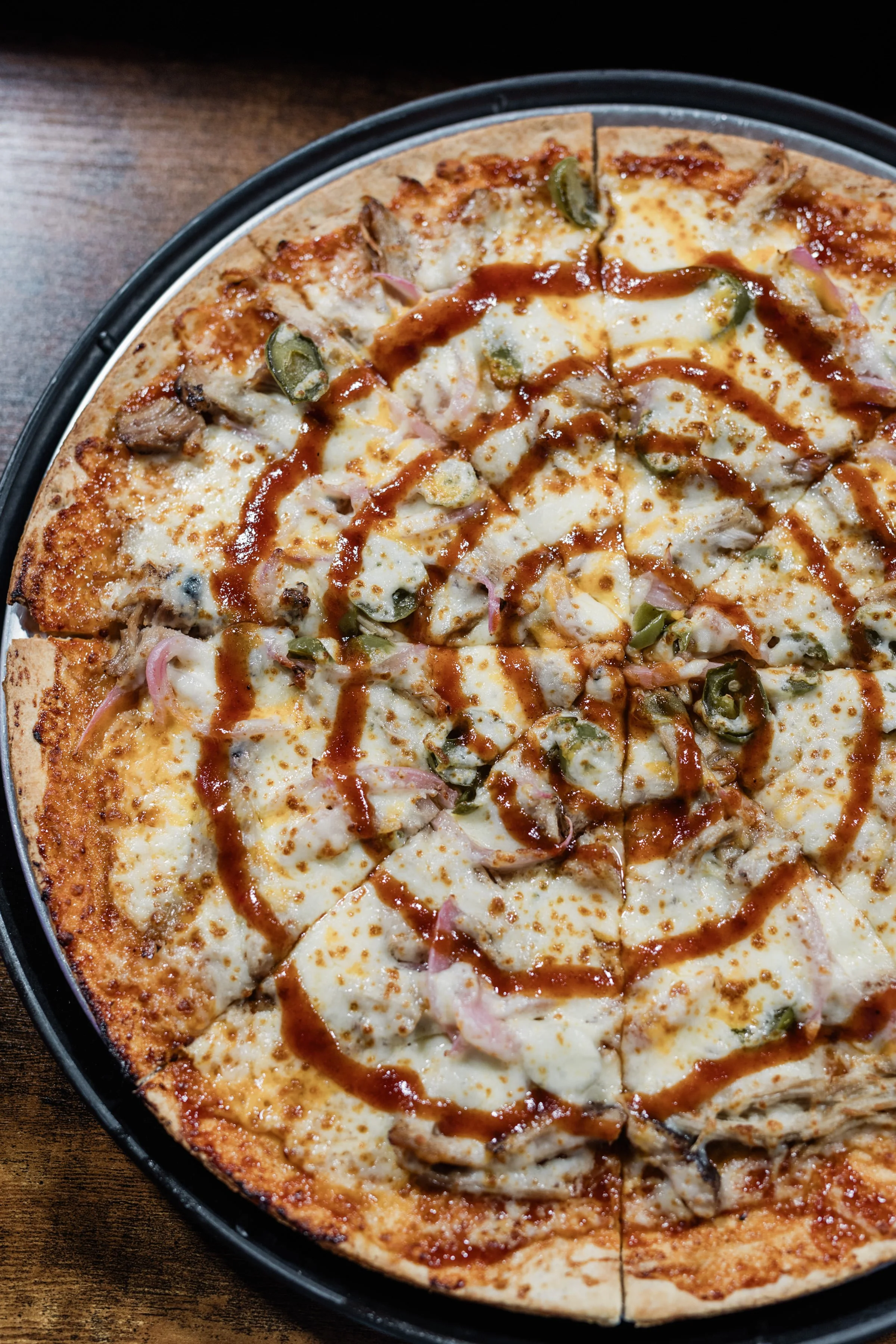 A pizza with cheese, green peppers, onions, chicken, and a drizzle of barbecue sauce on top.