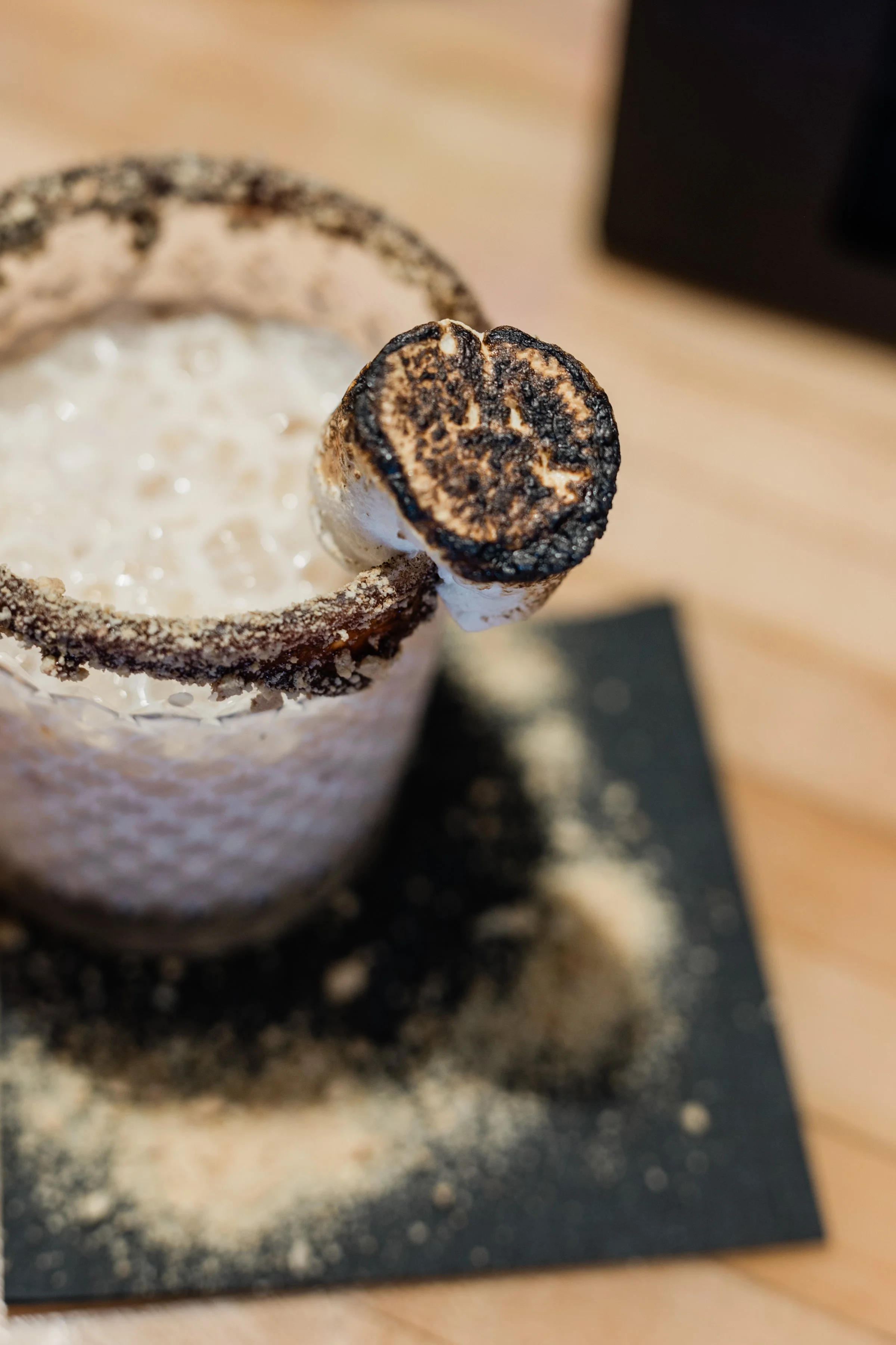 Close-up of a fancy chocolate drink with a toasted marshmallow on top, in a textured chocolate rim glass.