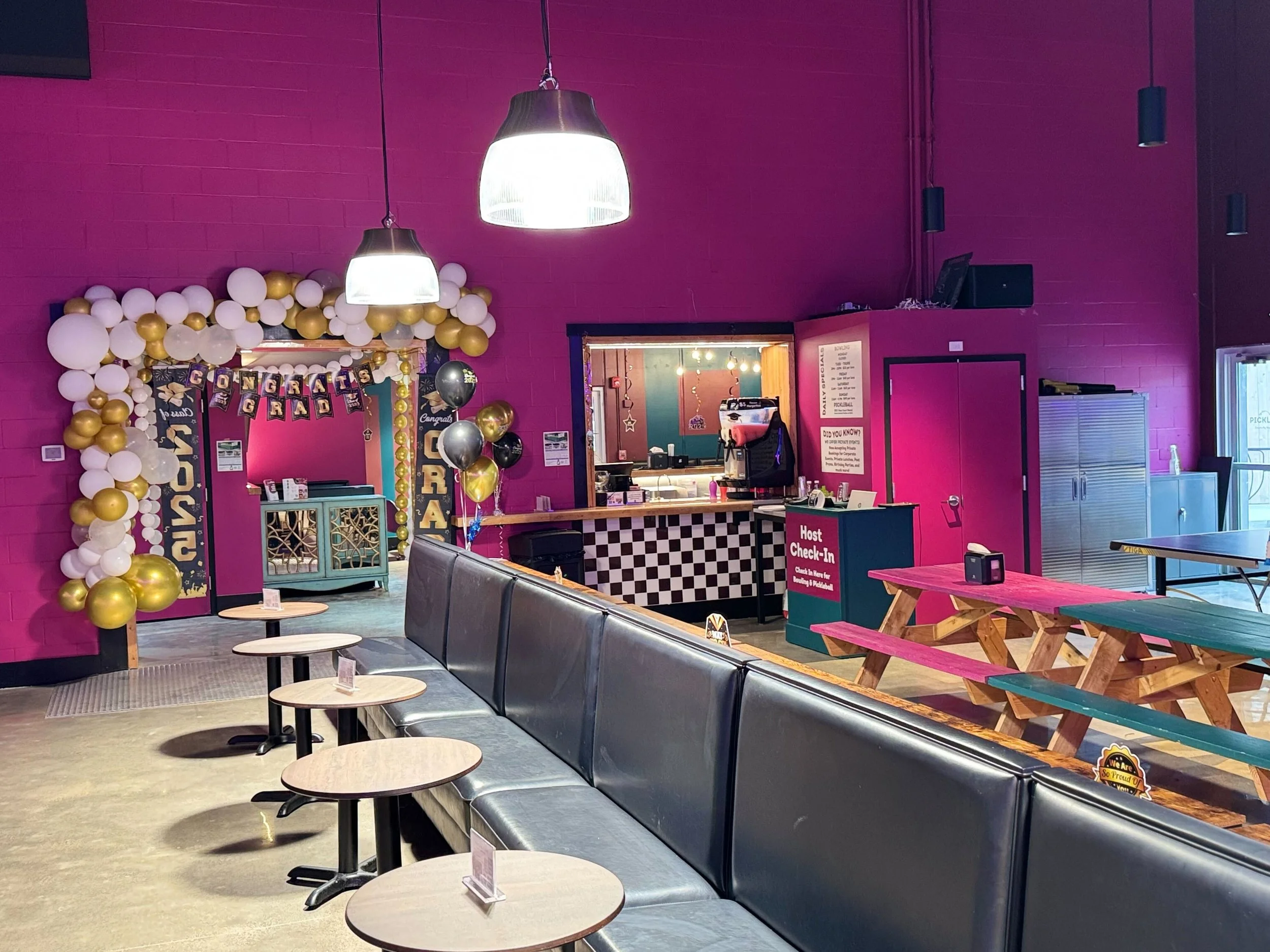 Colorful indoor space decorated with balloon arch, balloons, banners, and tables, with a check-in counter and seating area.
