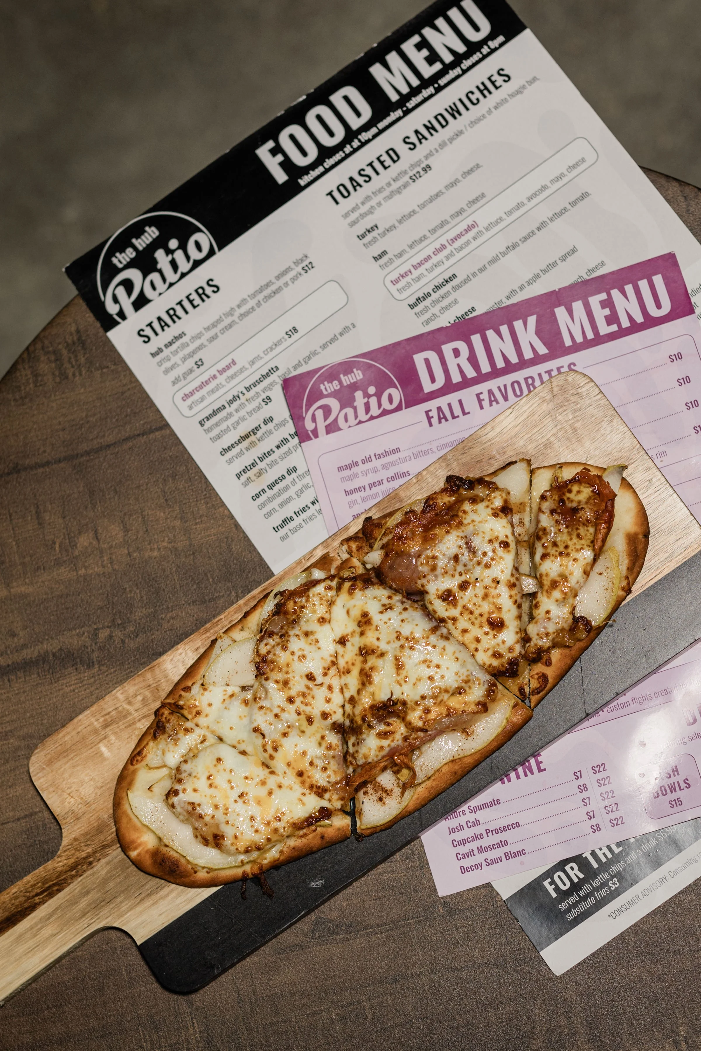 Cheese pizza on a wooden paddle placed on a table with menus underneath.