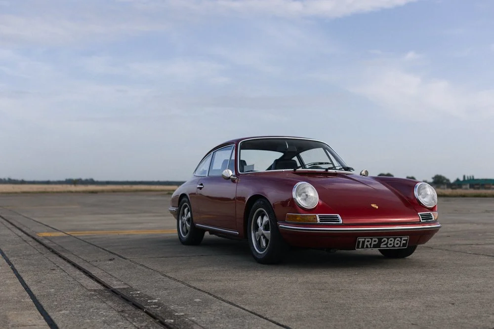 A classic red Porsche 911 car parked on an empty runway or tarmac under a cloudy sky.