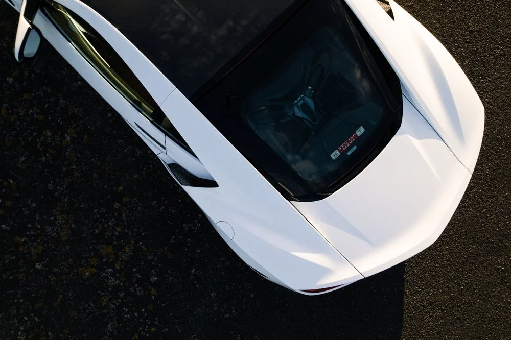 A white sports car parked on a dark, textured surface, seen from above at an angle.