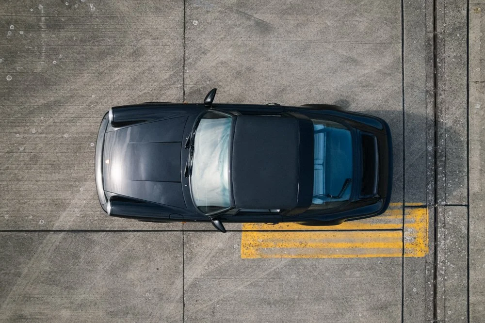 Black sports car parked on a concrete surface with yellow parking lines.